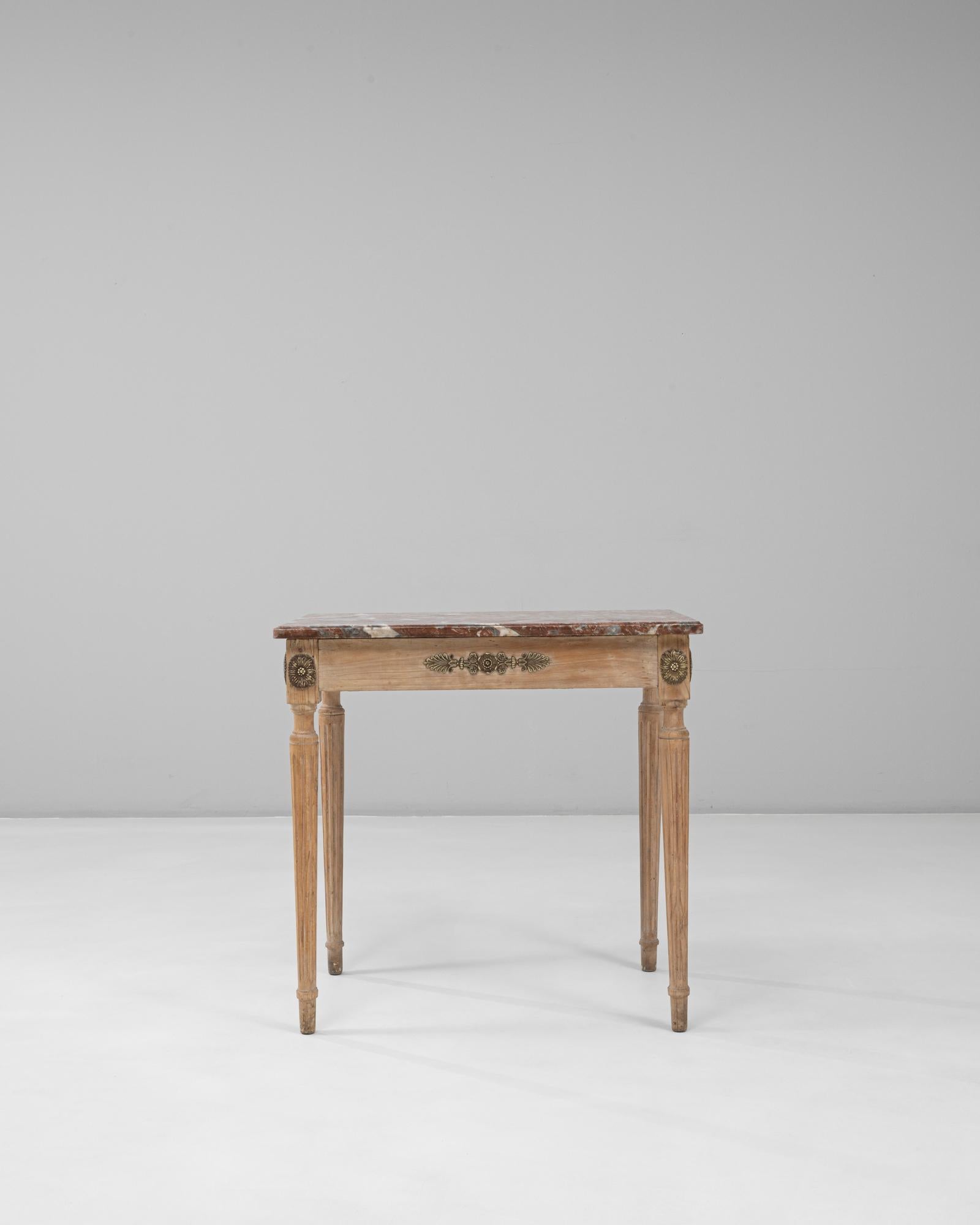 This 20th-century French Louis XVI side table embodies the timeless elegance of neoclassical design. Crafted from carved wood with a lightly patinated finish, it features fluted tapered legs and refined gilt-bronze rosettes and floral appliqués. The