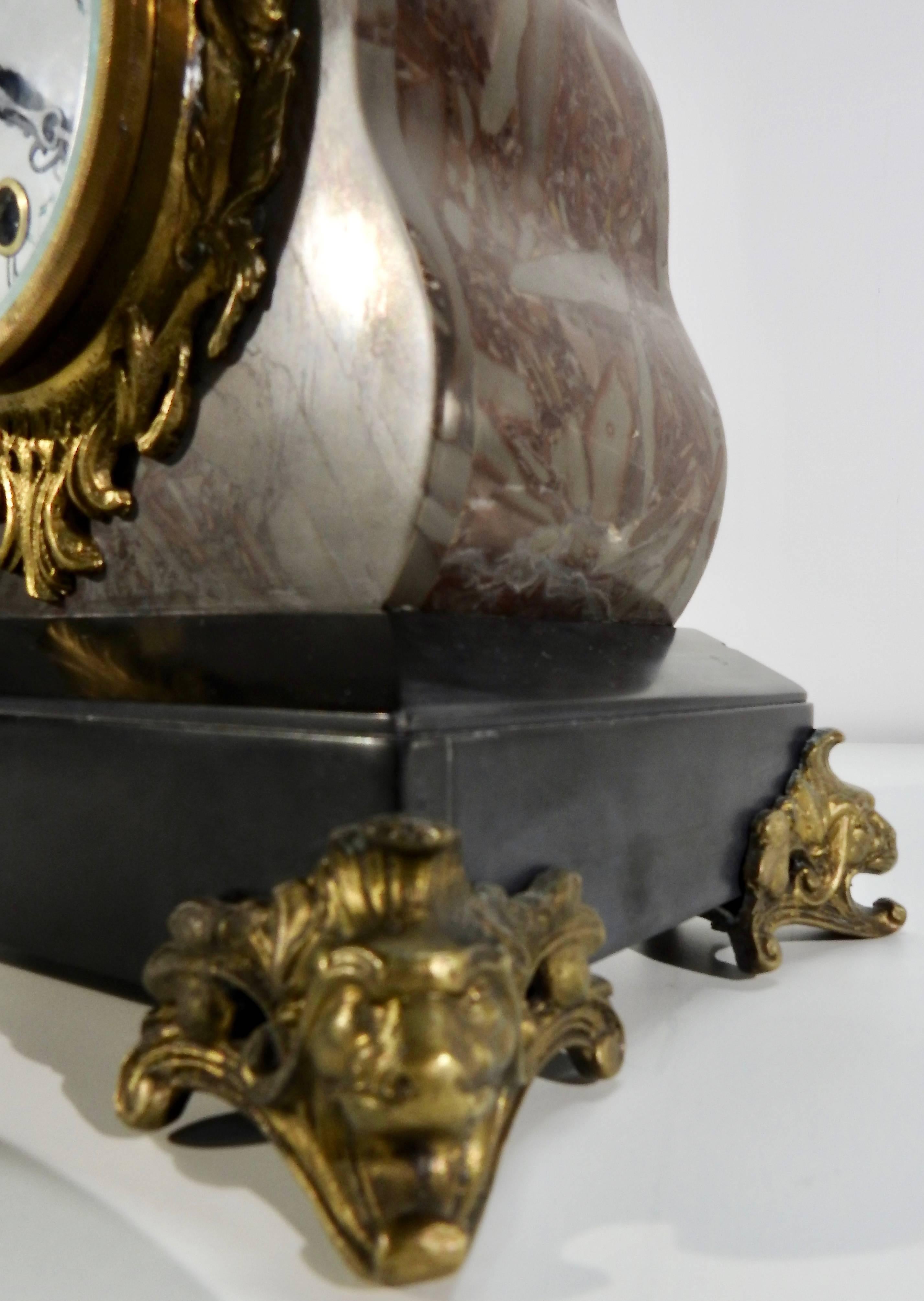 A stunning bronze cherub sits at the place of honor at the top of this French mantel clock. The body of the clock is made of marble with veins of gray and burgundy. It is completed with Classic black slate. There is beautiful bronze metal work