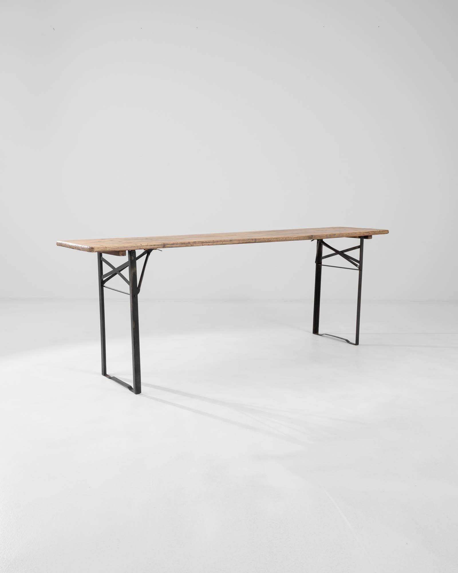 A metal table with a wooden top created in 20th century France. Spry and wiry, this crafty table exudes a sense of industrious yet handmade creativity. Metal elements are welded together in a geometric network buttressing each end of the table,