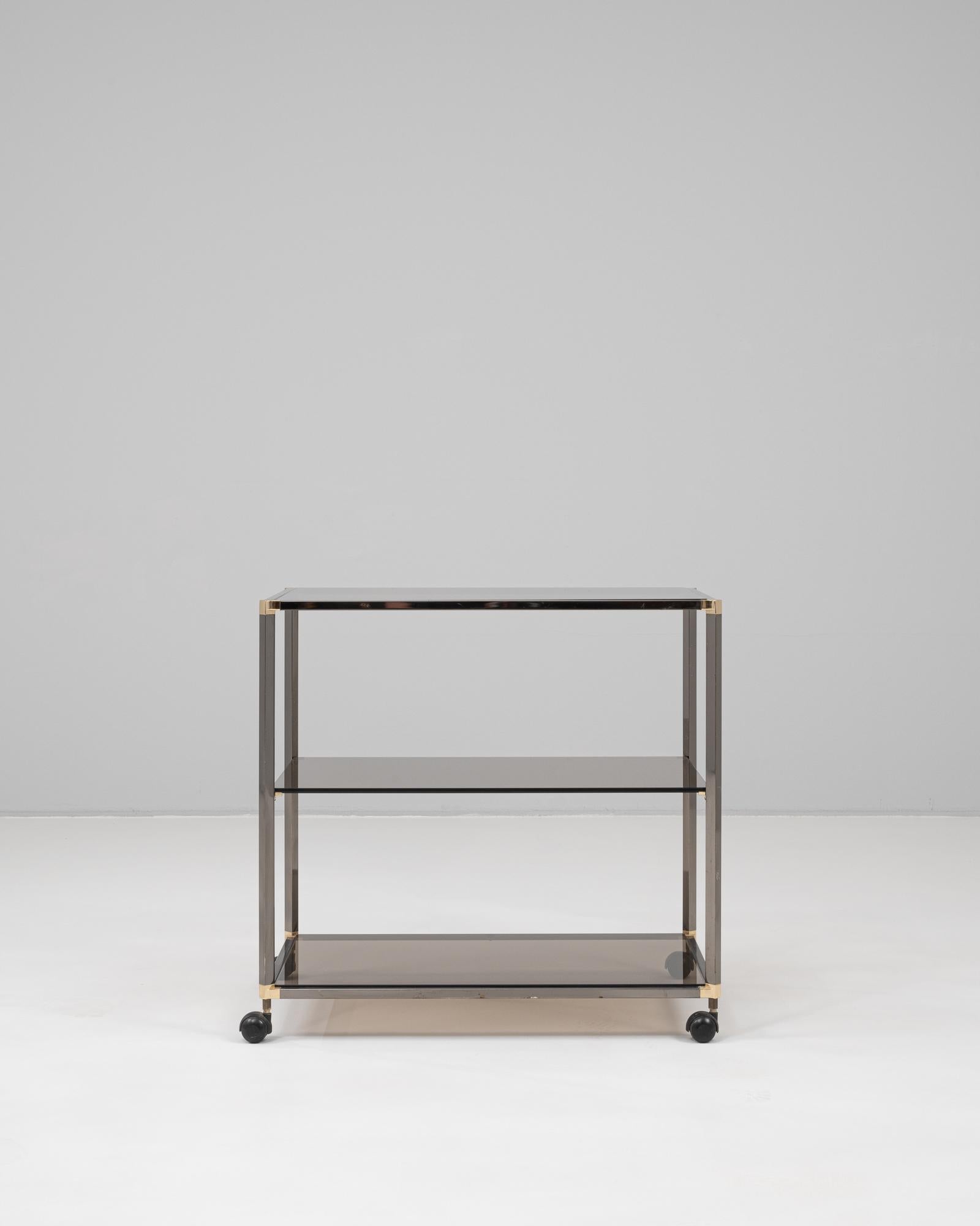 This 20th Century French bar cart showcases a sleek, minimalist design that merges function with refined modernism. Constructed with a polished metal frame and three tiers of smoked glass shelving, the cart offers ample surface space for serving or
