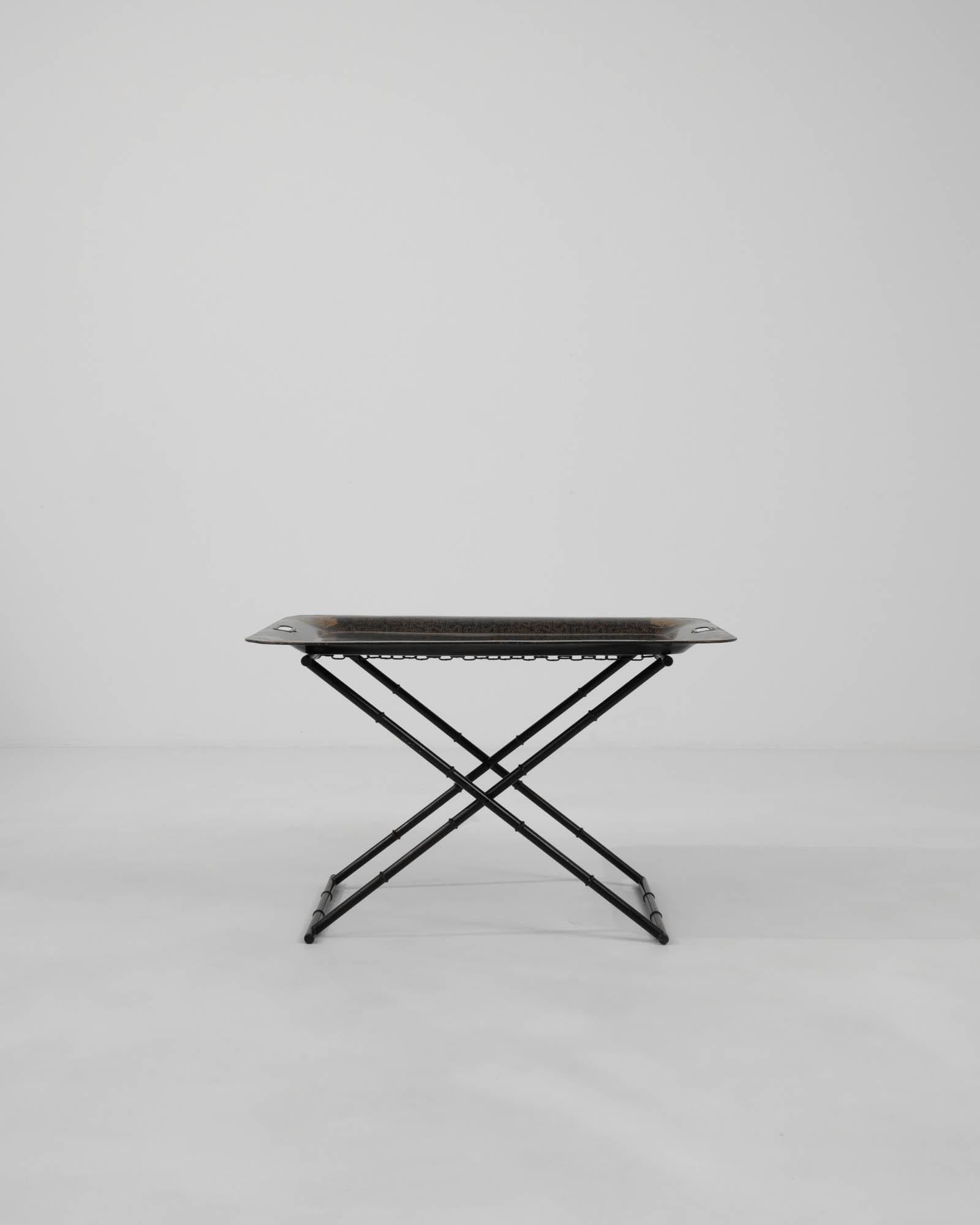 Présentant la quintessence de l'ingéniosité française et du design du XXe siècle, cette table basse pliante en métal allie l'aspect pratique à une touche artistique. Le cadre en métal noir est conçu pour être à la fois solide et élégant. Il est doté