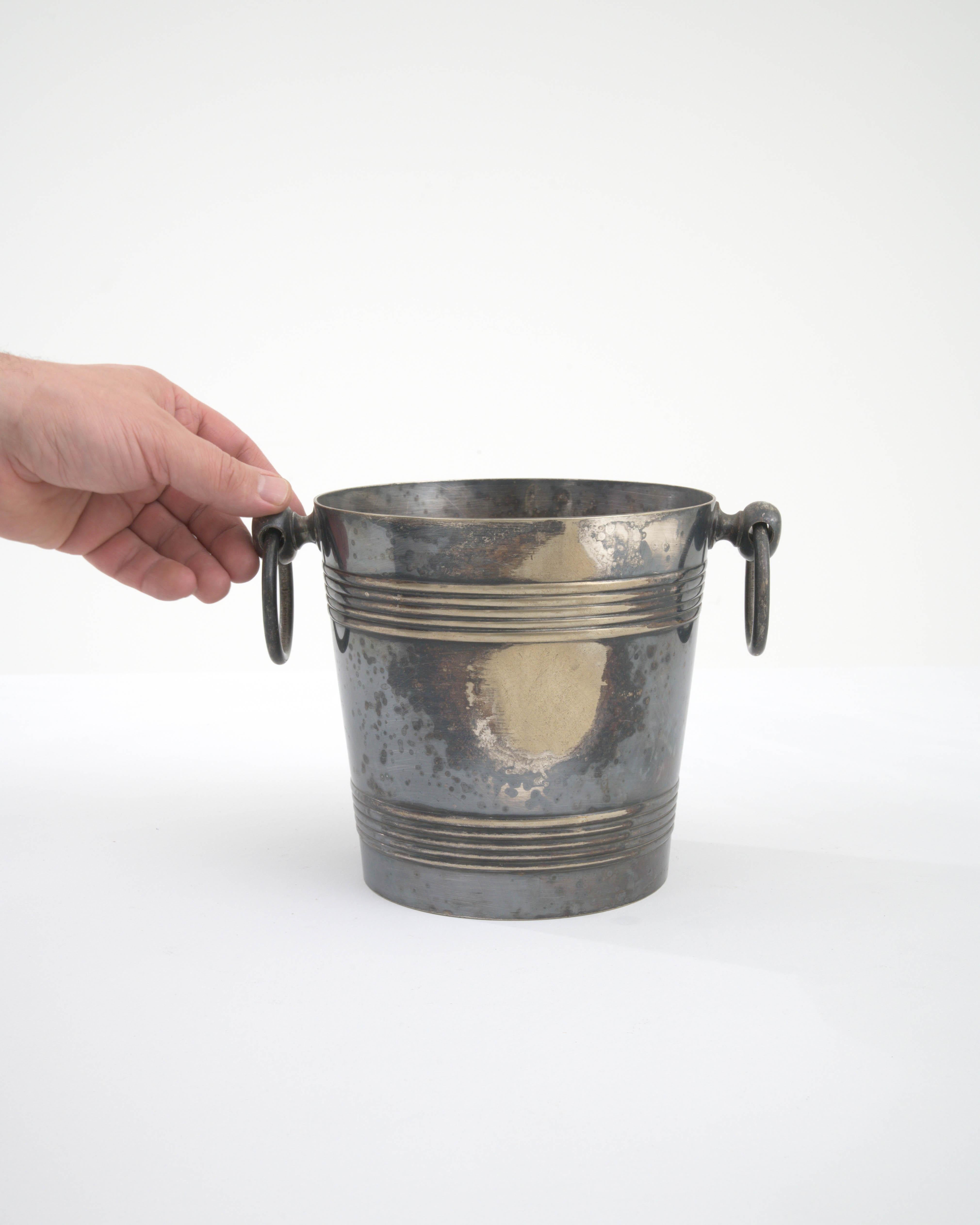 Experience the fusion of utility and vintage charm with this 20th Century French Metal Ice Bucket, a perfect addition to your sophisticated soirées. The bucket's galvanized metal construction promises durability and an authentic patina that whispers