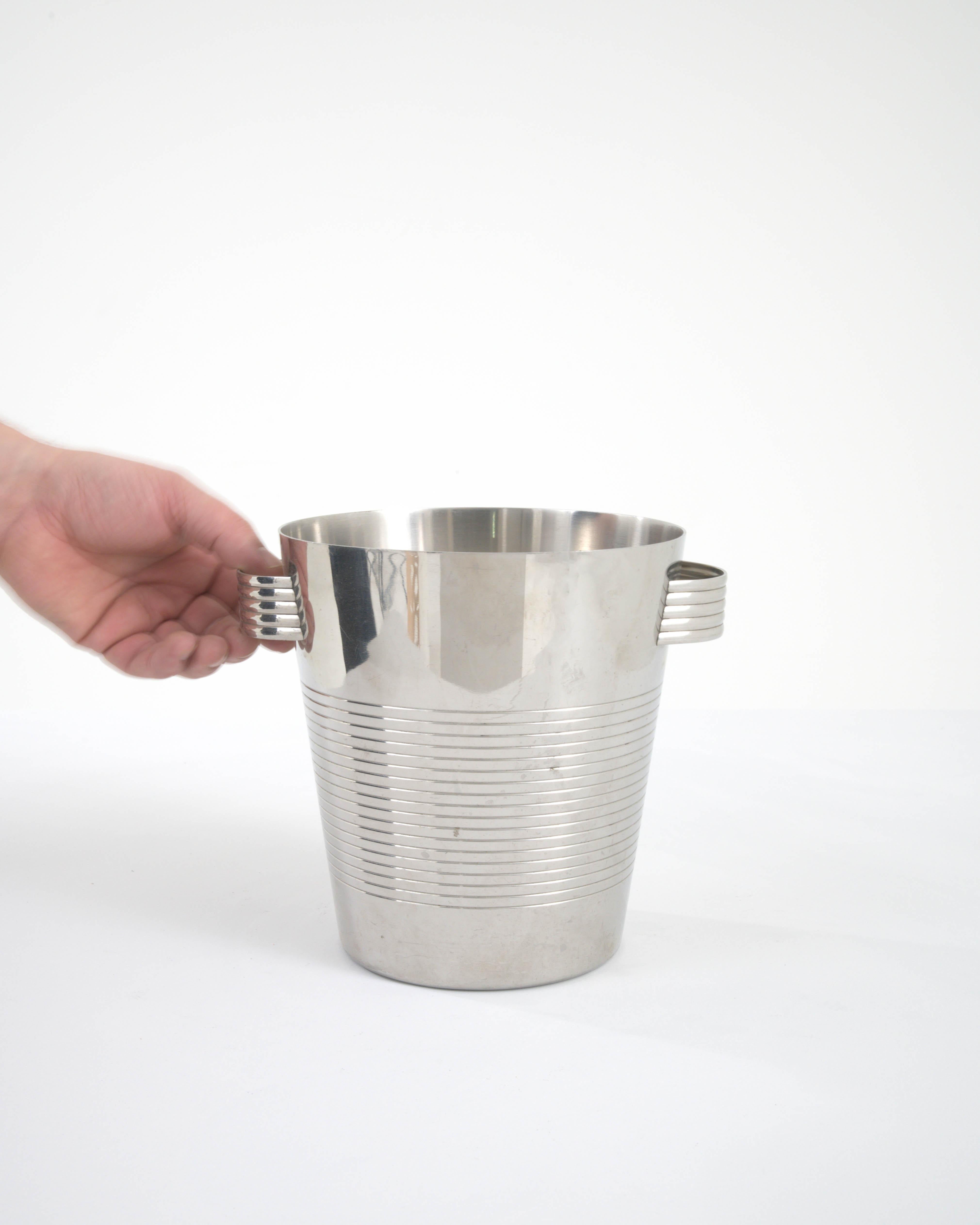 This 20th Century French Metal Ice Bucket presents a seamless blend of functionality and elegance. The sleek, brushed metal finish paired with the clean lines of the bucket's form exudes a modern yet timeless charm. Notable for its ribbed detailing,