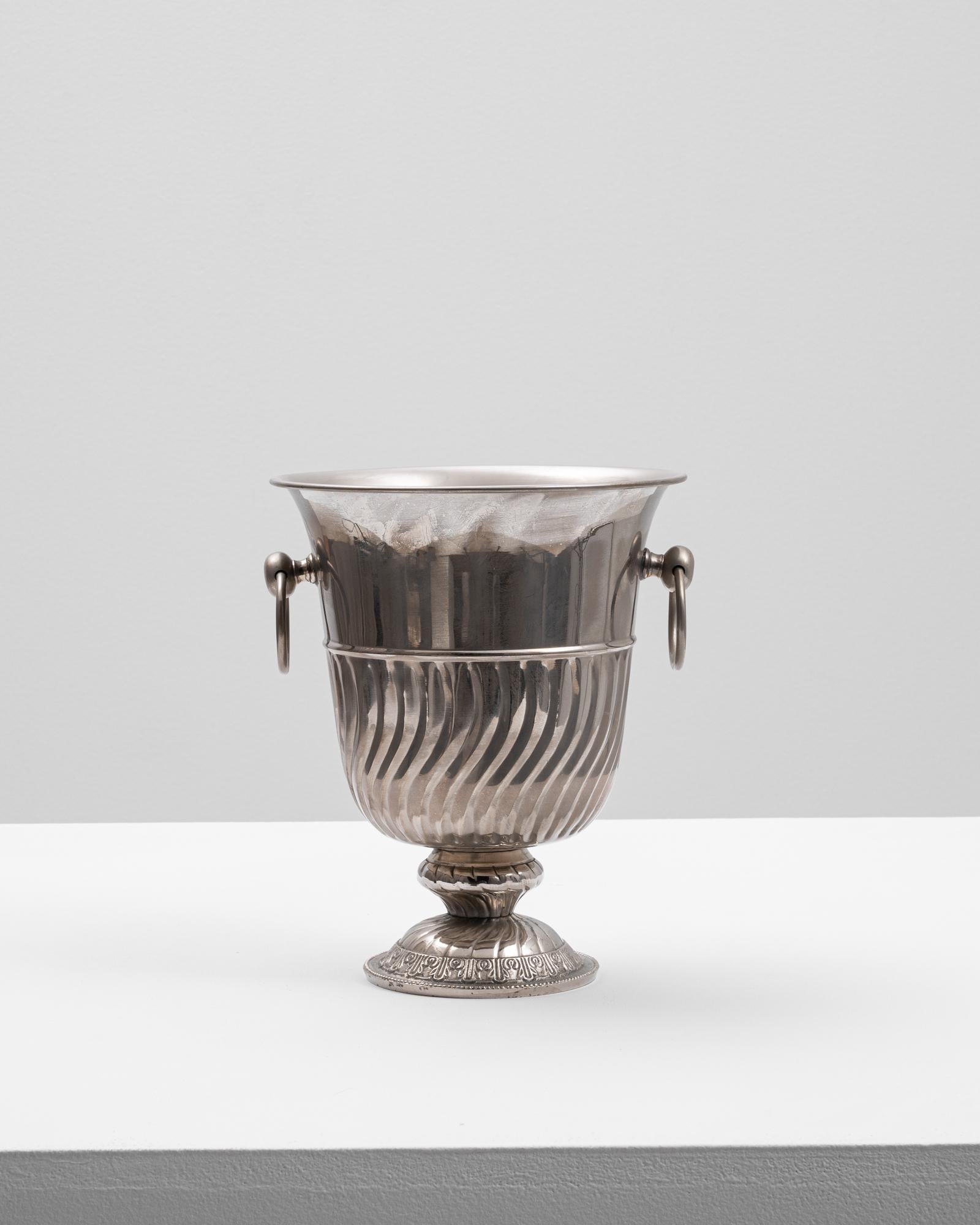 This 20th Century French metal ice bucket is a refined example of classic barware, blending decorative detail with functional elegance. Crafted from polished metal, the bucket features a flared rim, twisted fluting along the body, and two round side