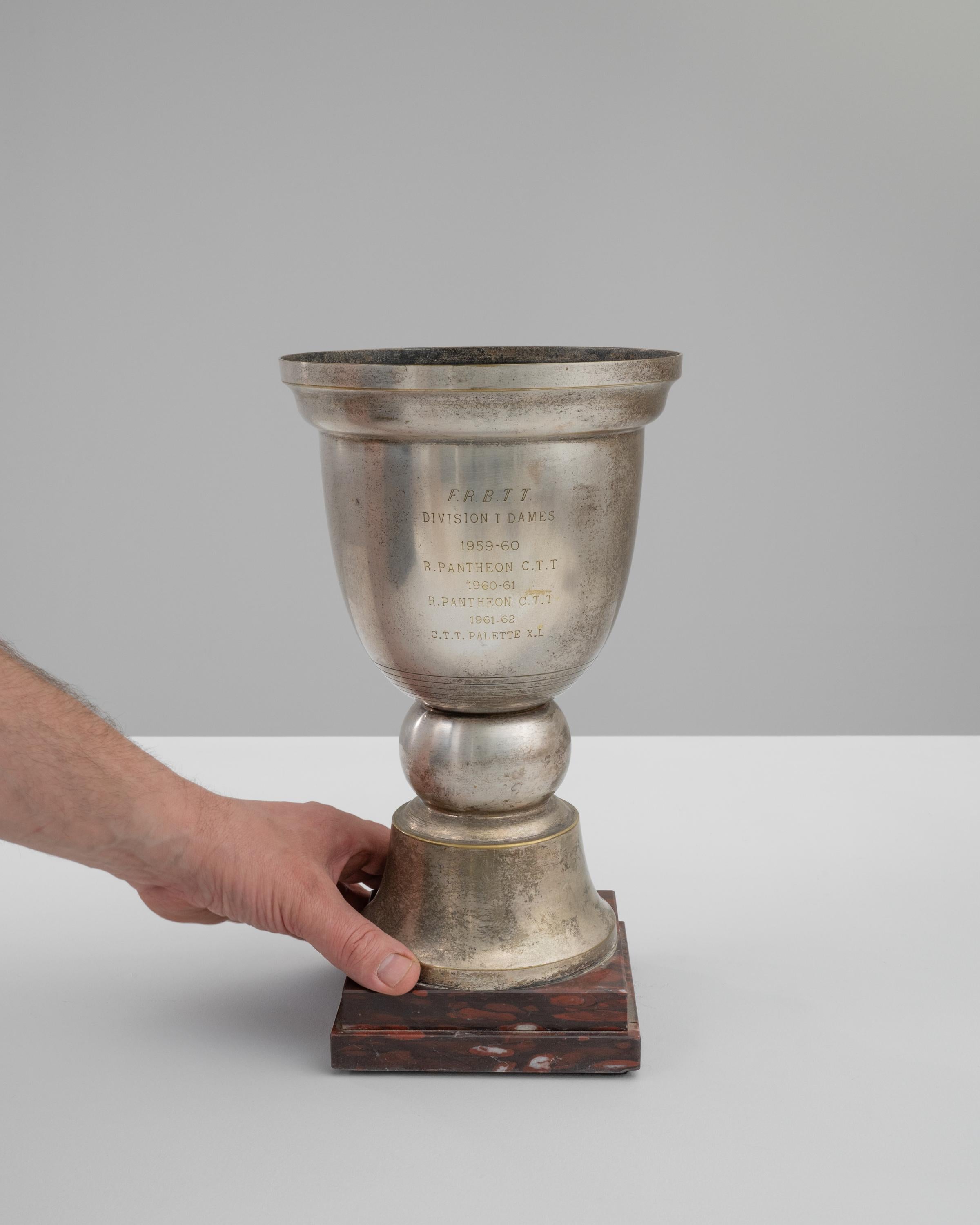 Versetzen Sie sich mit dieser prächtigen französischen Pokal-Trophäe aus dem 20. Jahrhundert in die Vergangenheit zurück - ein wahres Zeugnis für sportliche Höchstleistungen und historische Sportereignisse. Dieser aus glänzendem Metall gefertigte