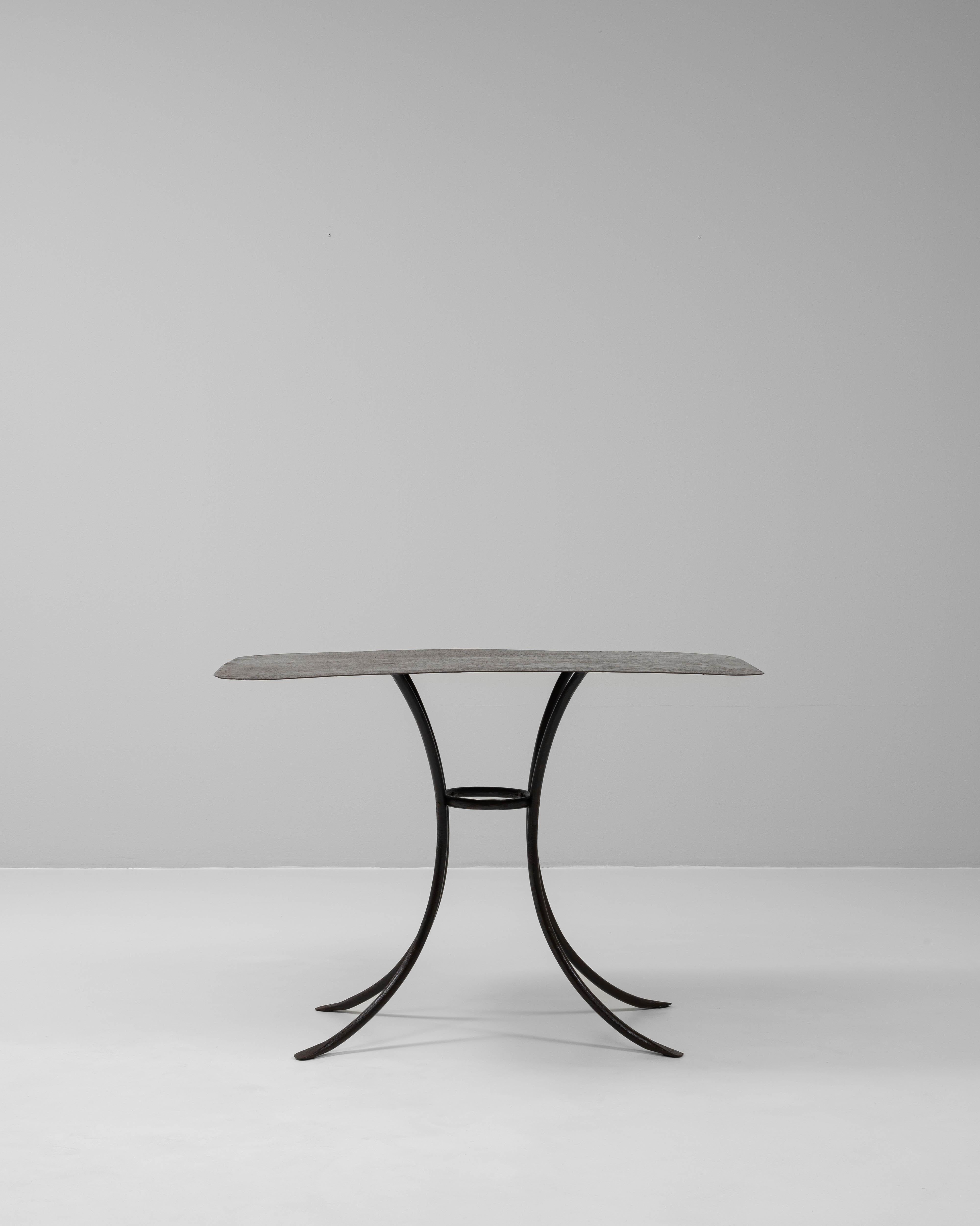 This 20th-century French metal side table exemplifies elegant minimalism with a distinctly architectural presence. Crafted from wrought iron, the design features four gracefully curved legs that converge at a central circular brace, offering both