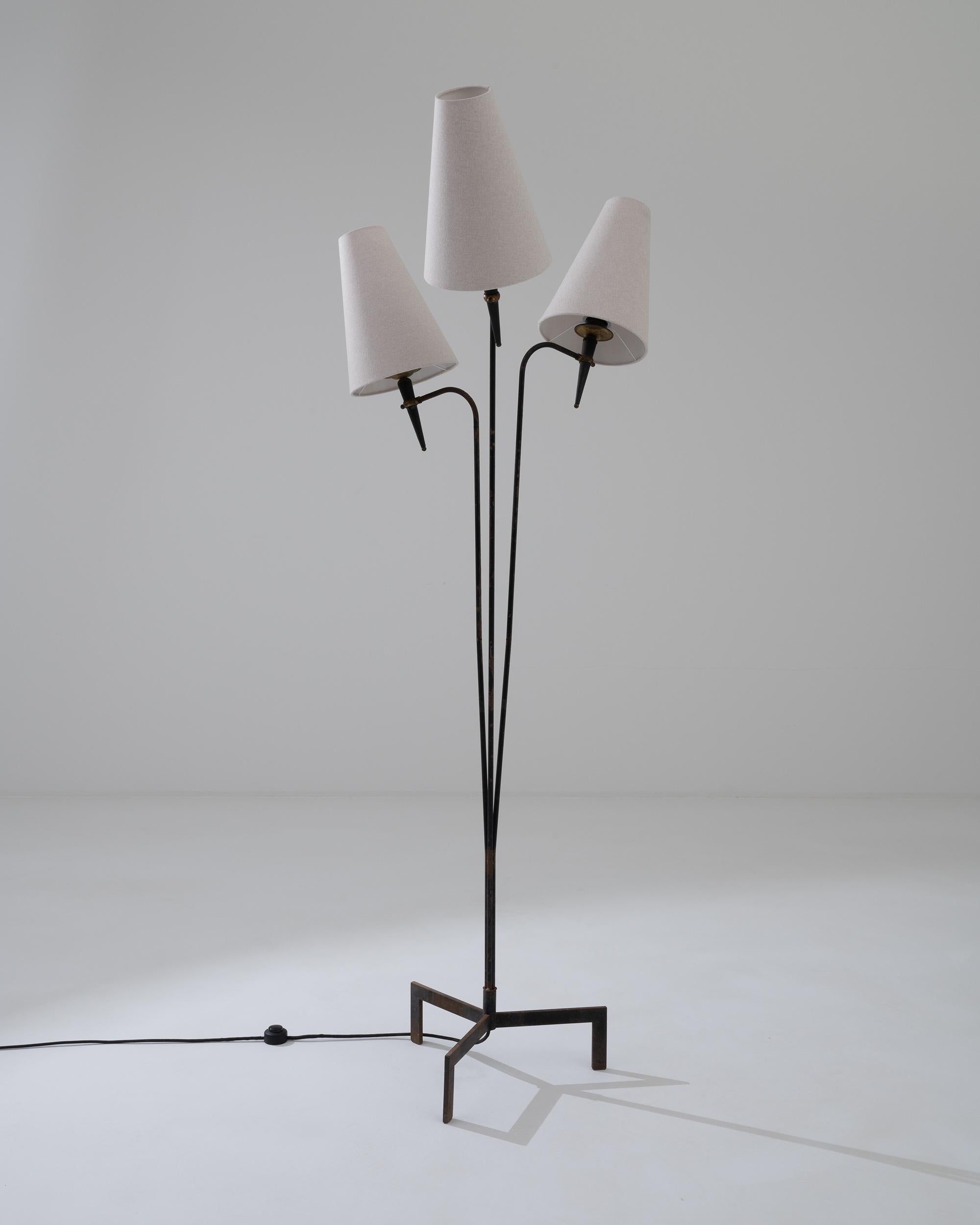 This distinctive floor lamp, designed in France during the 20th century, features a unique tripod structure with three lights that playfully emerge from a three-legged metal base. The triangle-shaped white lampshades are supported by gracefully