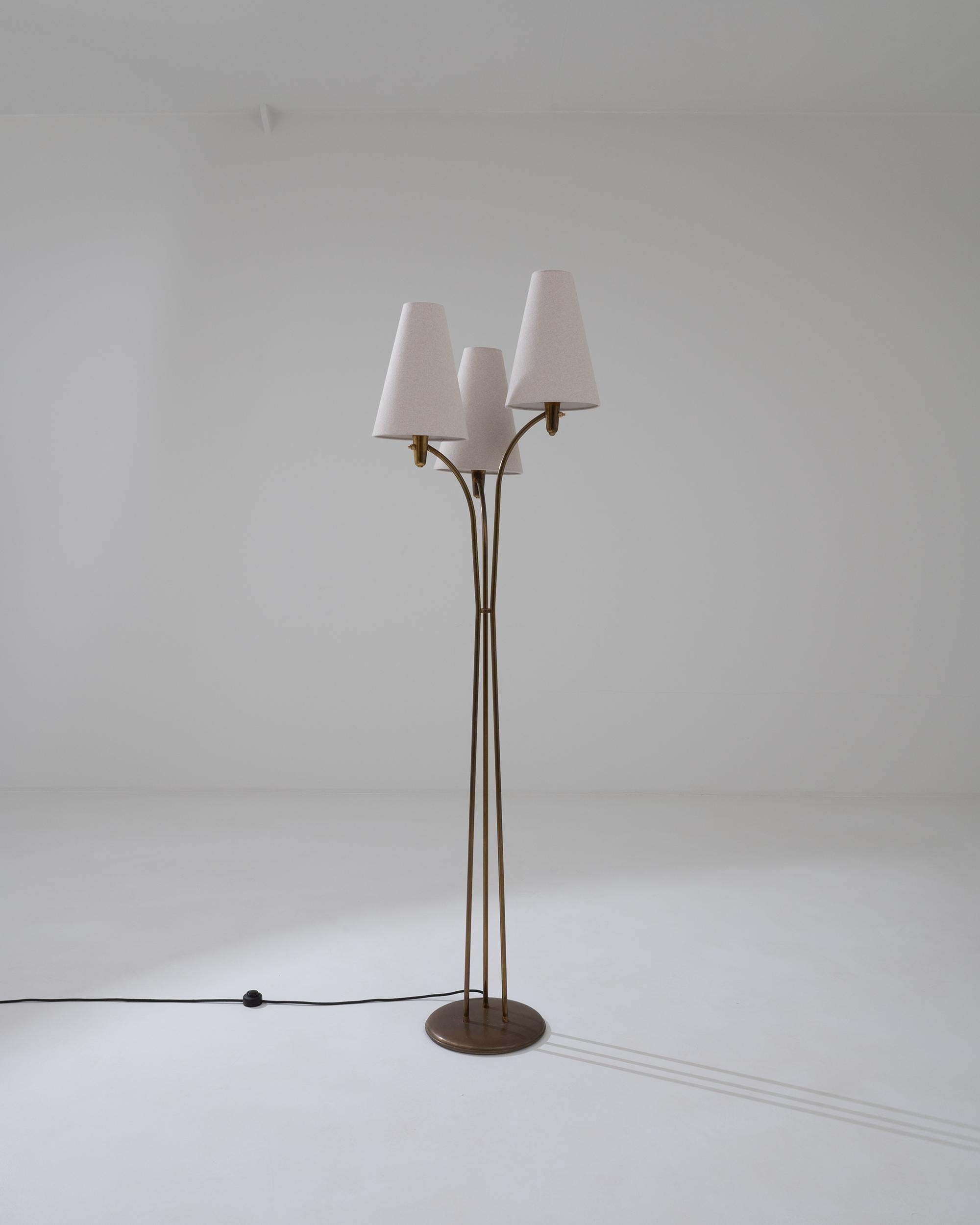 This distinctive floor lamp, designed in France during the 20th century, features a unique tripod structure with three lights that playfully emerge from a circular metal base. The triangle-shaped white lampshades are supported by gracefully inclined