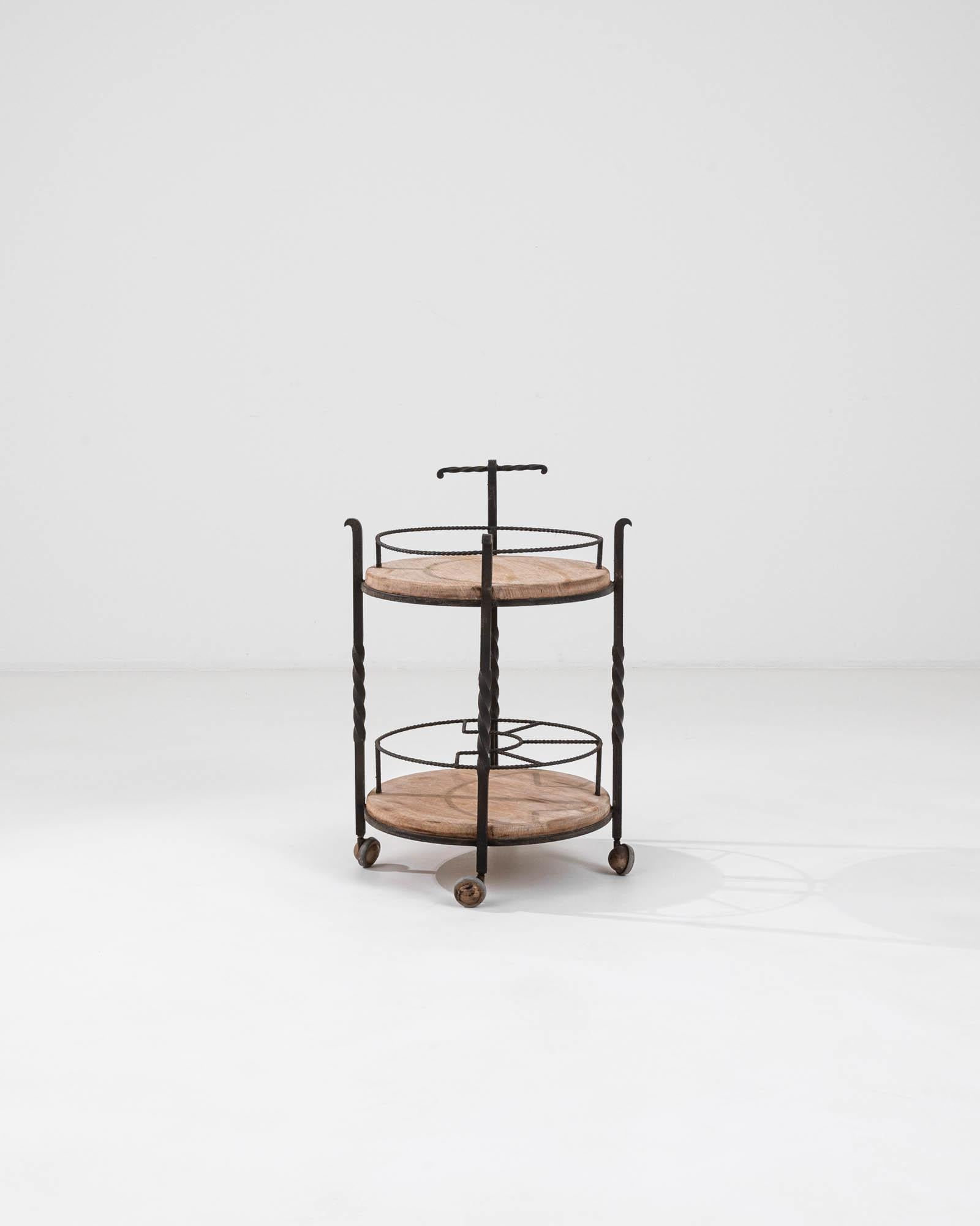 Delight in the vintage charm and functionality of this 20th Century French Metal & Wooden Bar Cart. Crafted with a discerning eye for style, this cart features an elegant marriage of warm wood and wrought iron, delivering both beauty and utility to