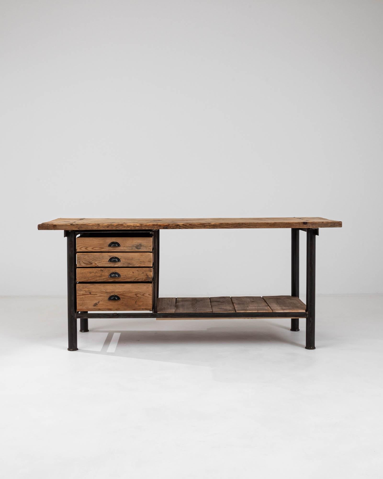 This sturdy and industrial 20th Century French Work Table merges functionality with the raw aesthetic of its era. The robust metal frame provides a solid foundation, supporting the richly textured wooden top and shelves that exude character and