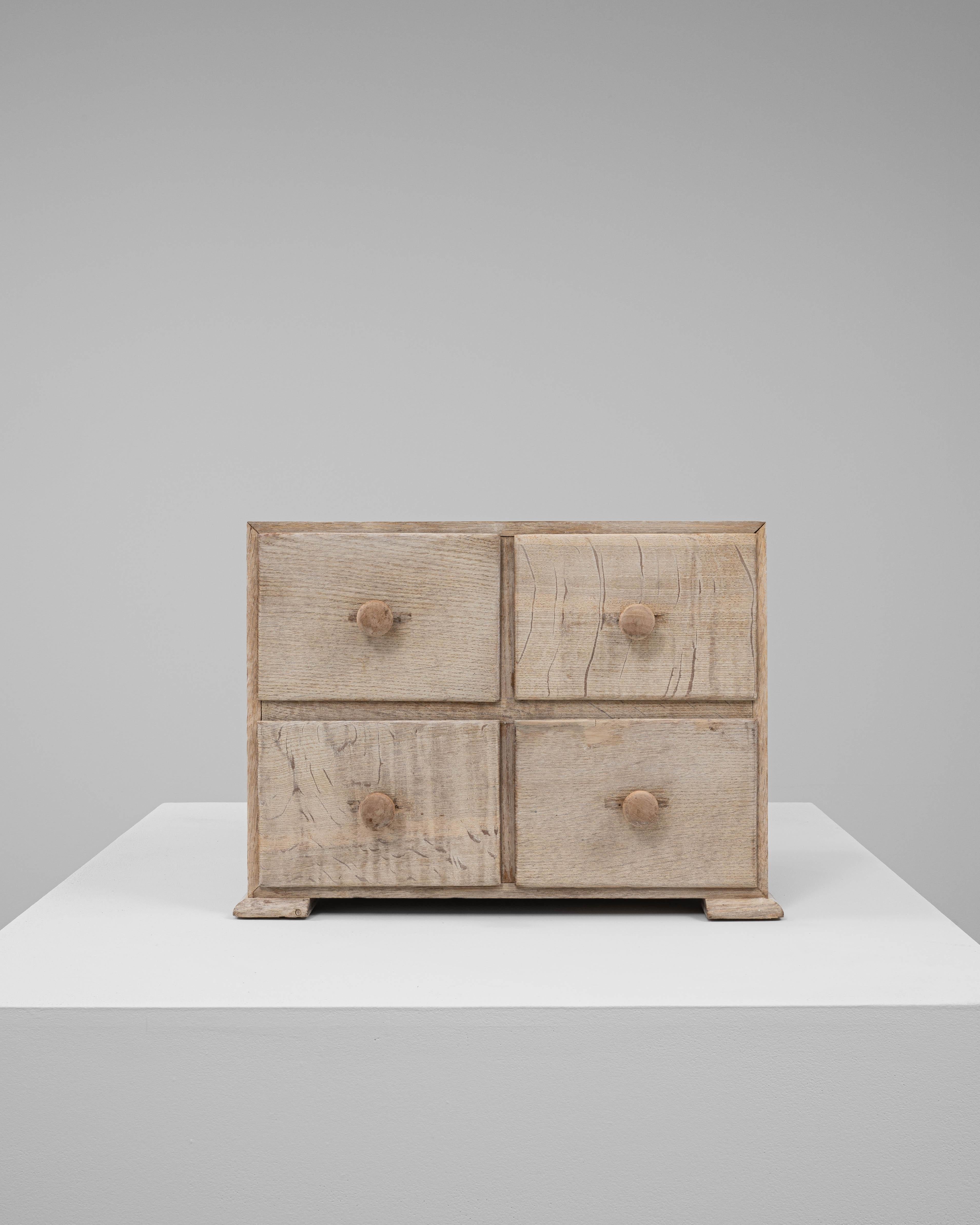 This 20th century French mini chest of drawers is a charming example of rustic craftsmanship, featuring a simple, functional design with four small drawers. Constructed from solid wood, it displays a light, natural patina that accentuates the grain