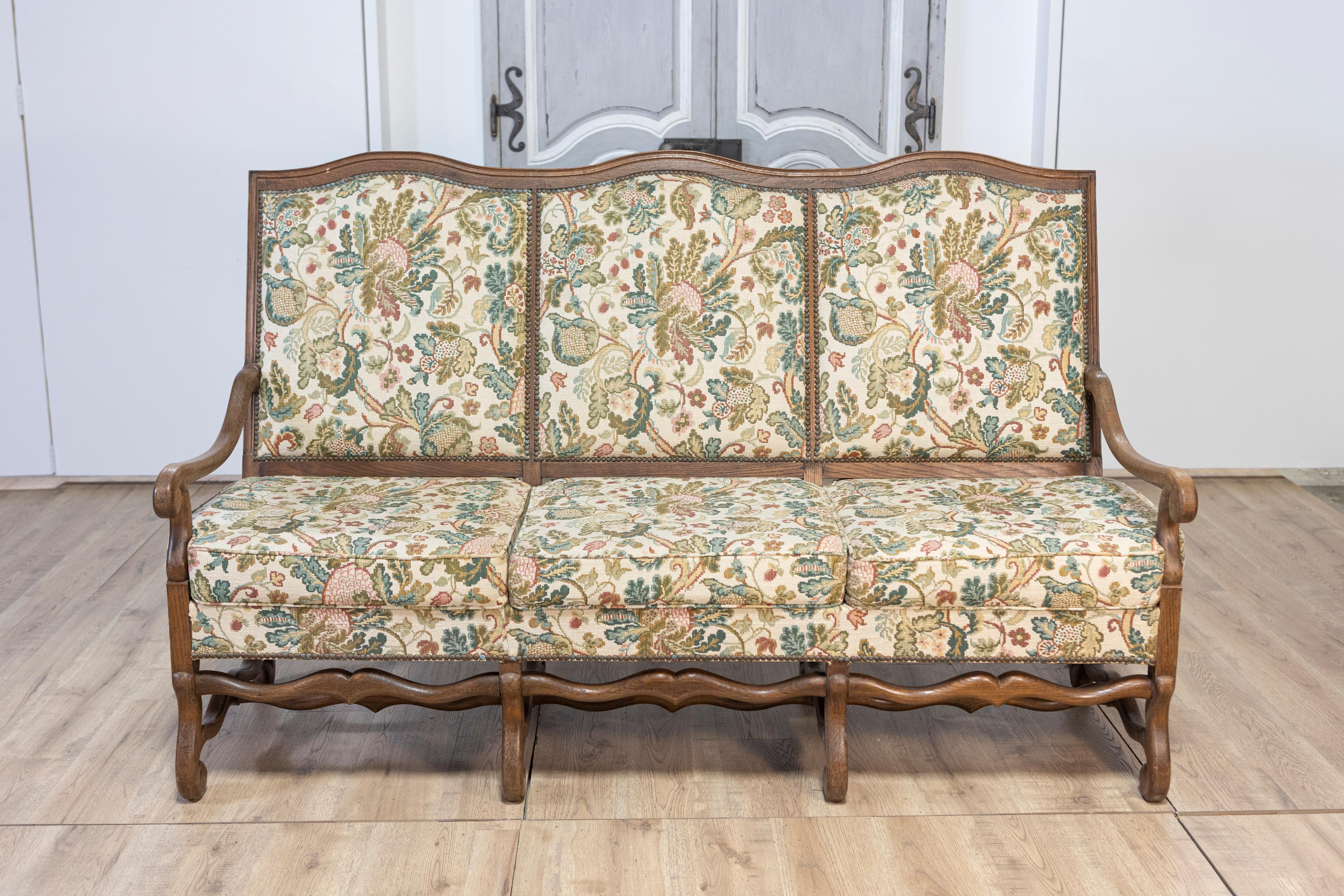 Questo squisito divano a gambe di montone in noce francese del XX secolo è un pezzo senza tempo del design provinciale francese. Realizzato in noce massiccio, presenta gambe di montone elegantemente intagliate e una cornice splendidamente sagomata