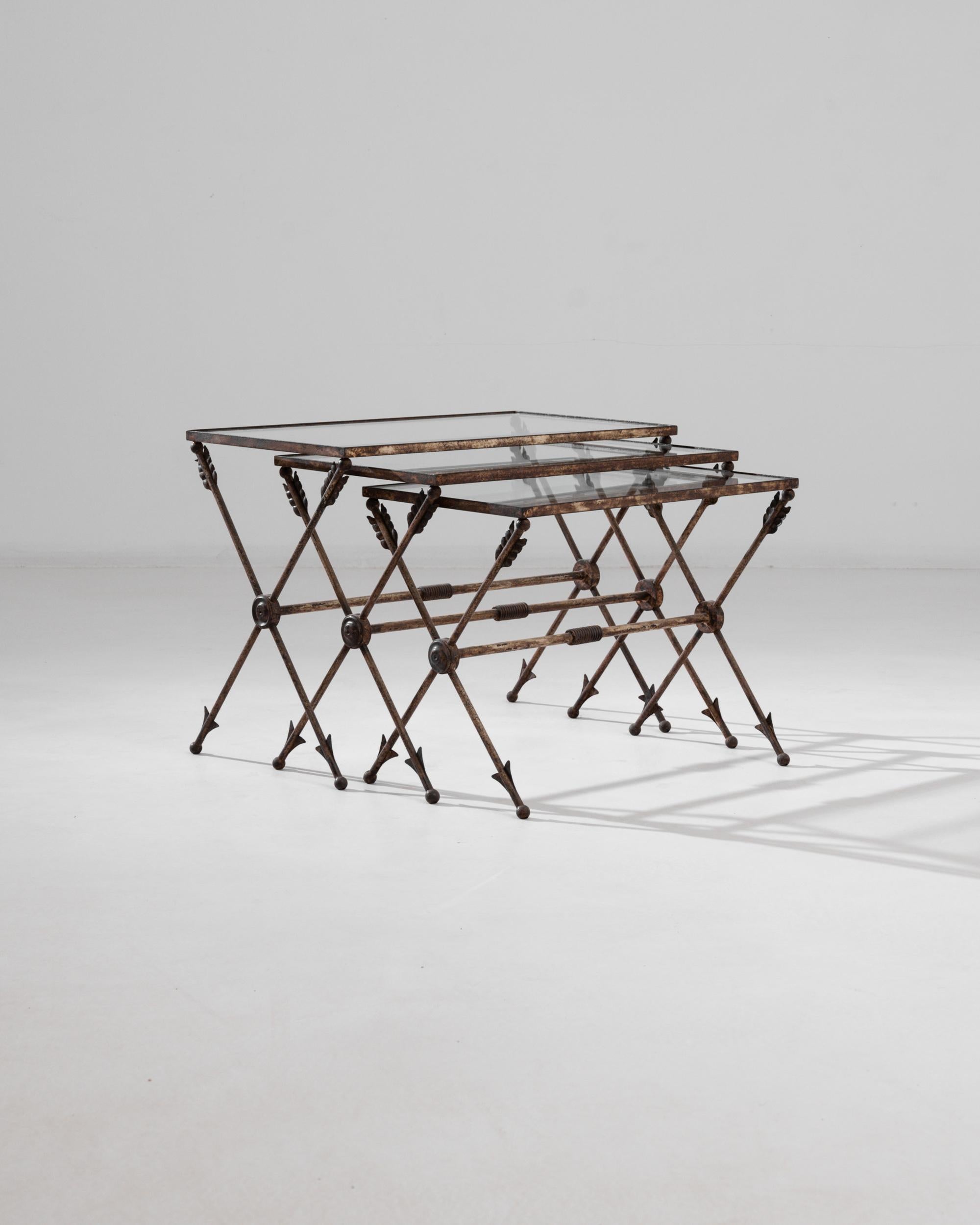 Made in 20th century France, this trio of nesting tables makes a unique vintage accent. A tabletop of transparent glass sits atop a slender metal frame, creating a lightweight and agile composition. The X-shaped legs are cast in the form of arrows,