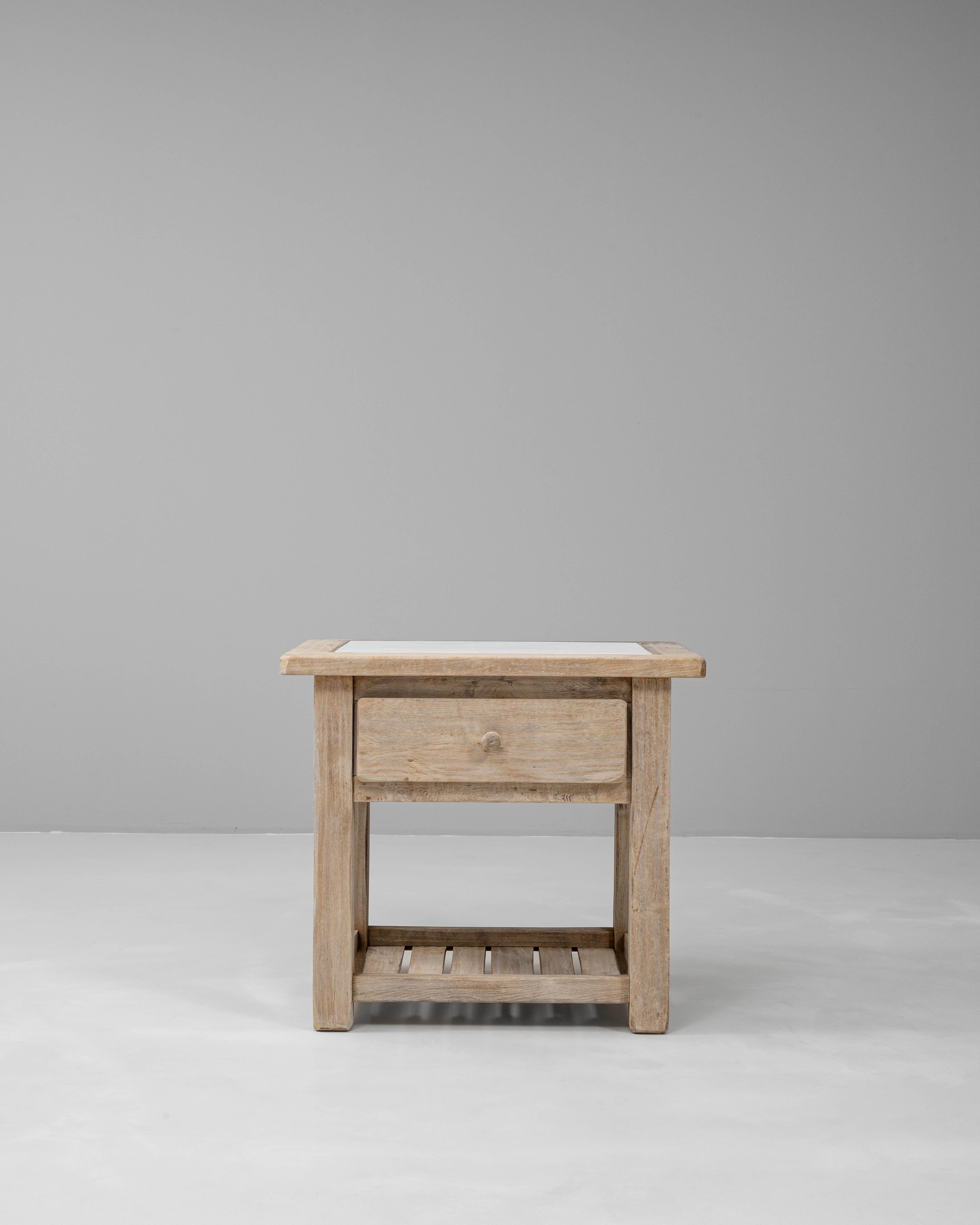 Table de chevet en chêne français du 20e siècle avec plateau en marbre, alliant charme rustique et savoir-faire raffiné. Le cadre en chêne massif présente une patine douce et naturelle qui met en valeur le grain et la texture du bois, tandis que la