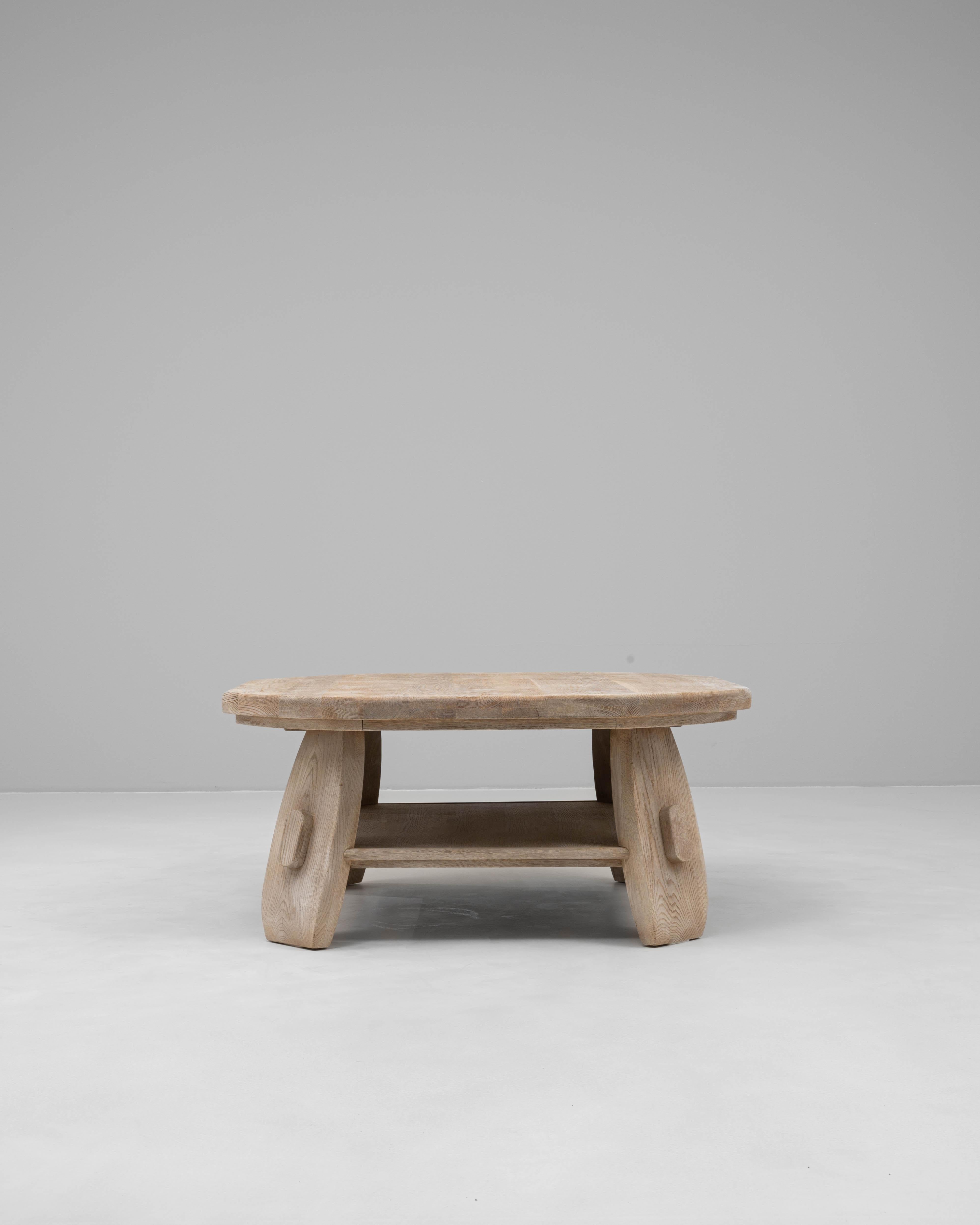 This 20th century French oak coffee table embodies a sculptural, modernist approach to traditional craftsmanship. Constructed from solid oak with a pale, natural finish, the table showcases a substantial, rounded top resting on boldly shaped legs