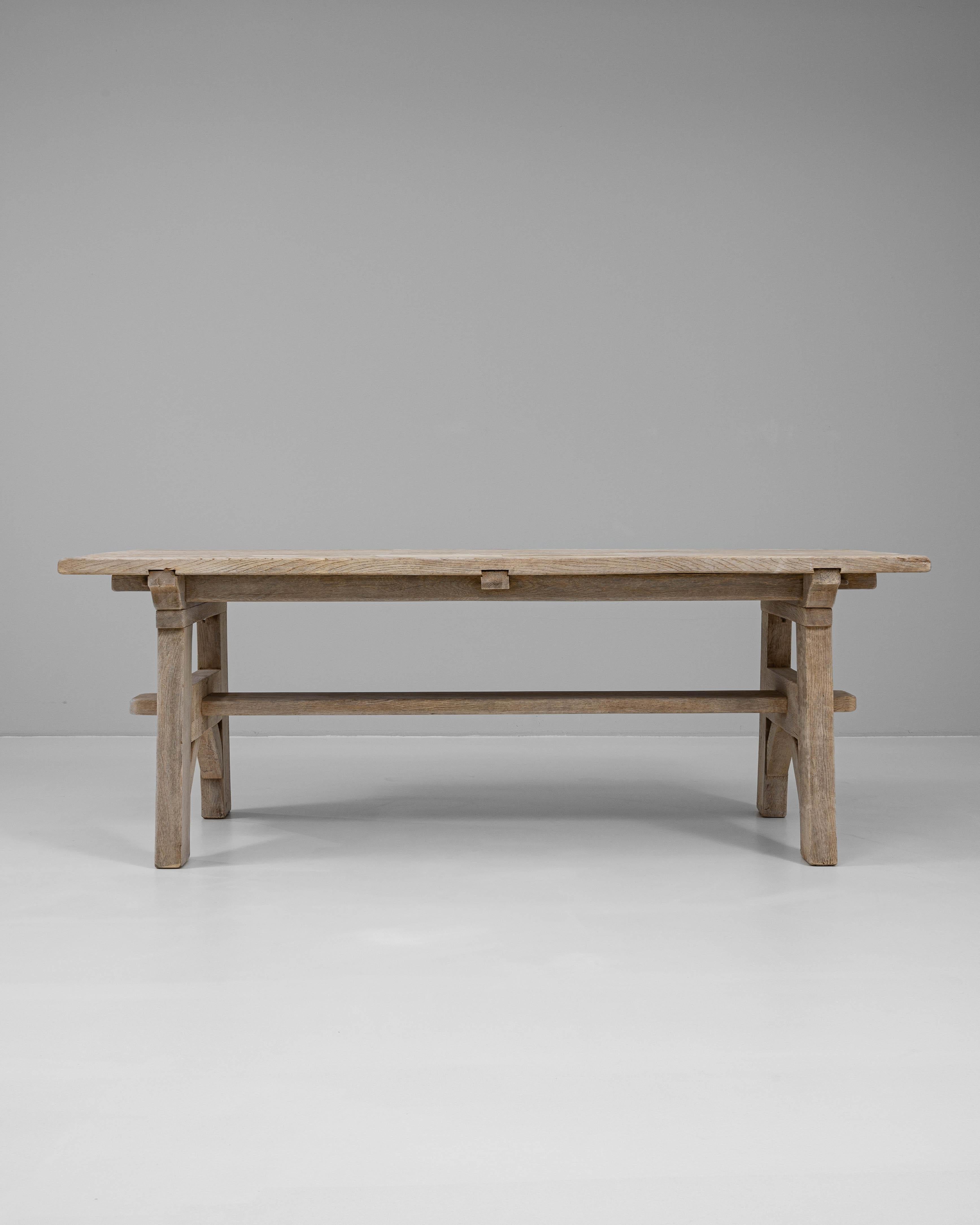 Esta mesa de comedor de roble francés del siglo XX ejemplifica la elegancia rústica con su construcción de madera maciza y su acabado natural. La robusta base de estilo caballete, unida por una robusta camilla, proporciona tanto estabilidad como una