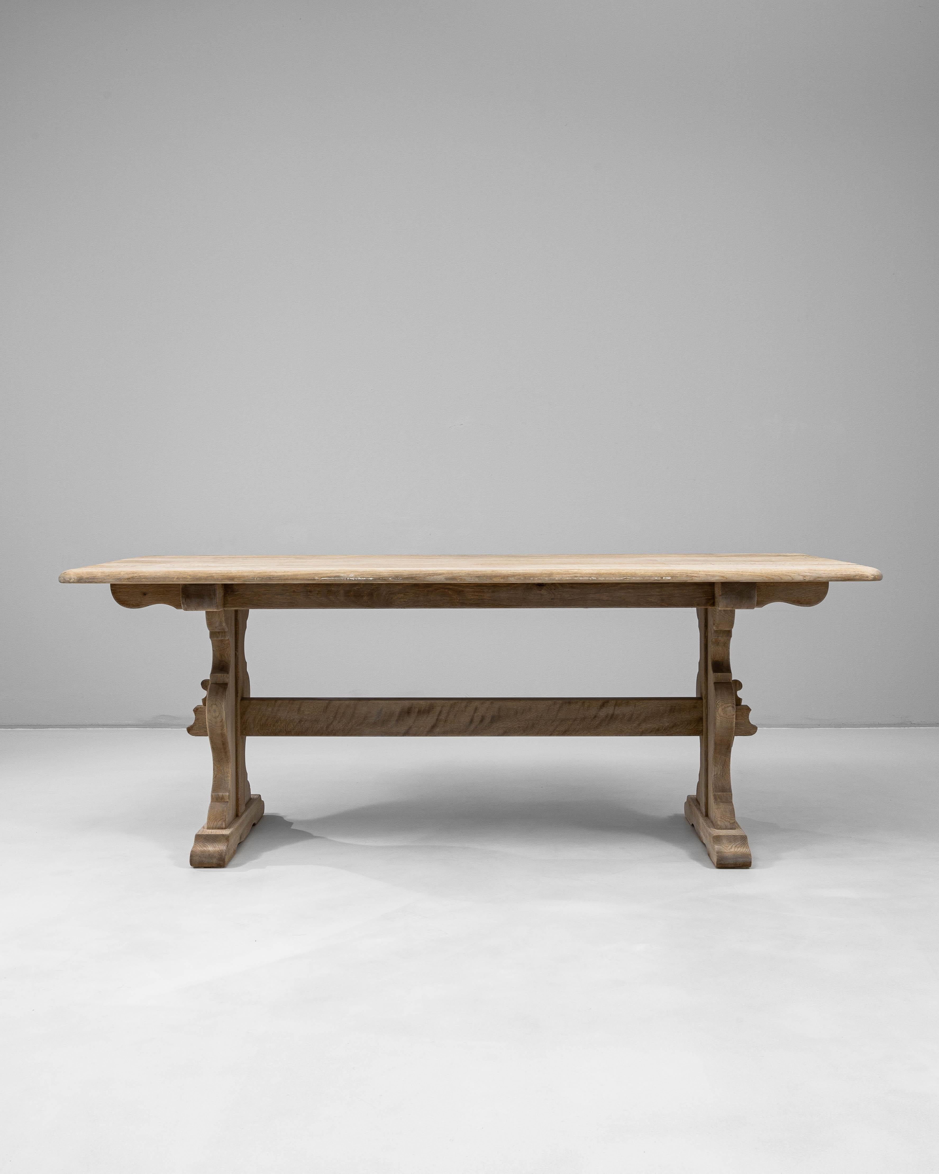 Un tavolo da pranzo francese scultoreo del XX secolo realizzato a mano in rovere massiccio. Lo spesso piano rettangolare presenta bordi ammorbiditi e poggia su due gambe piedistallo audacemente intagliate e unite da una barella per una maggiore