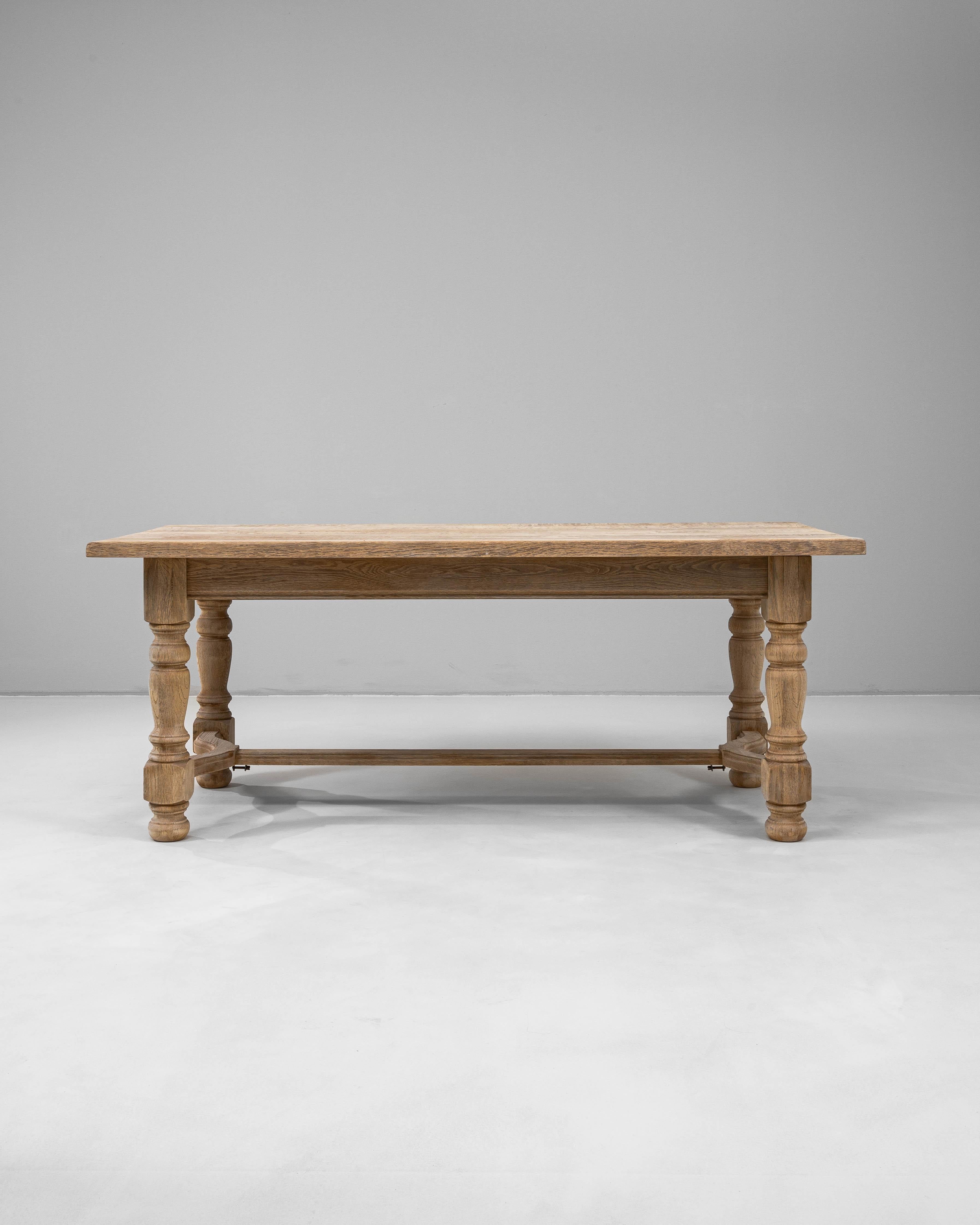 This 20th-century French oak dining table combines timeless craftsmanship with everyday functionality. Constructed from solid oak, it features a rectangular top with softly rounded corners and a finely textured surface that highlights the natural