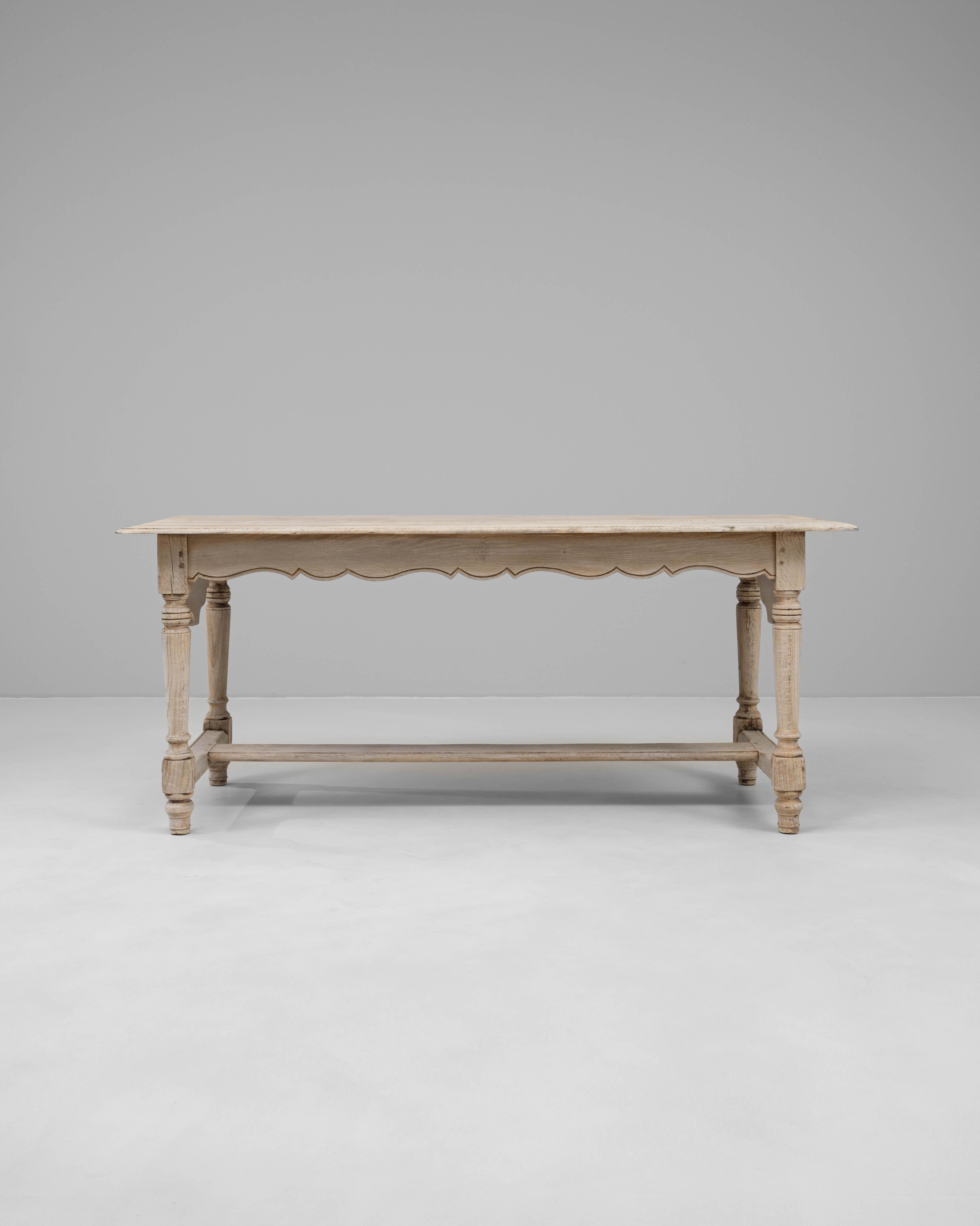 Table de salle à manger en chêne français du 20e siècle, d'une grande élégance, avec un tablier festonné et des pieds tournés reliés par une entretoise en H. La finition en chêne blanchi met en valeur le grain naturel et la texture subtile du bois,