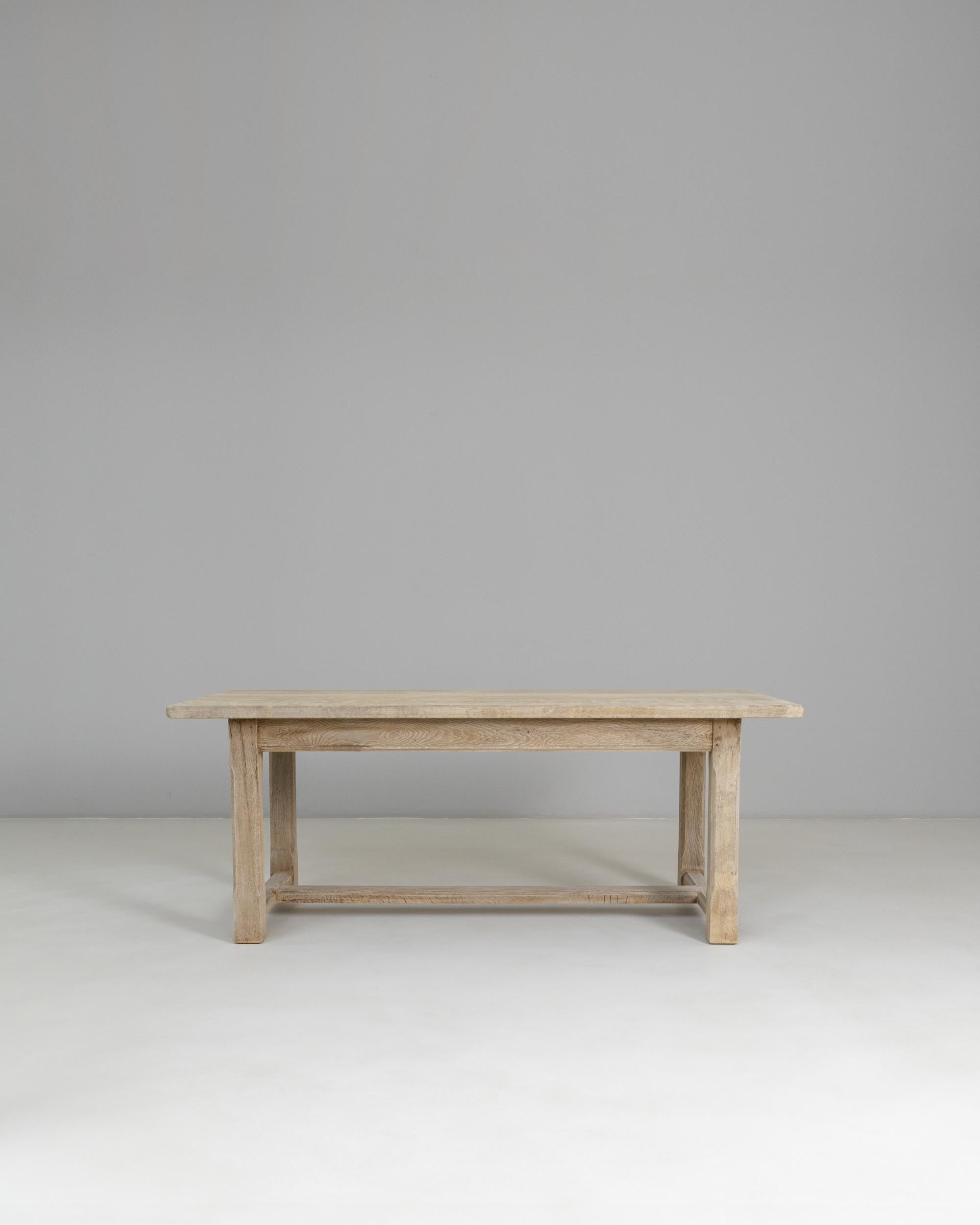 This 20th Century French oak dining table features a clean, understated silhouette that highlights the natural beauty and quiet strength of its solid oak construction. The rectangular top shows a soft, time-worn patina with visible grain patterns
