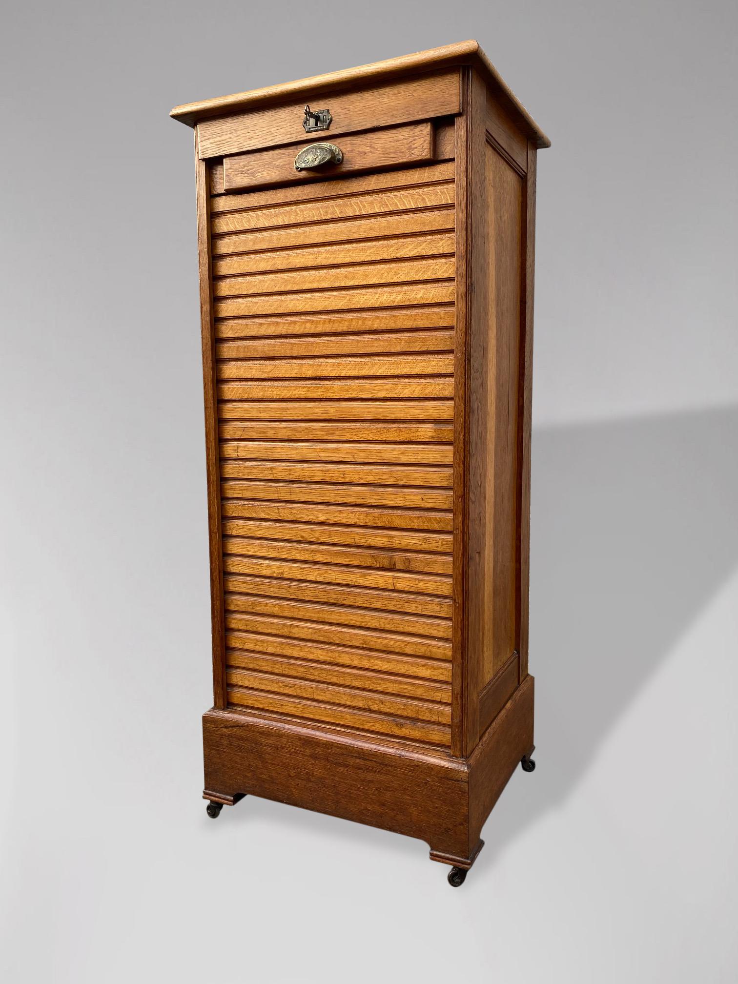 An early 20th Century French oak filing cabinet having a tambour roller shutter front, opening to reveal 9 internal pull out shelves, raised on a plinth base with small castors. In original condition with minor wear consistent of age and use