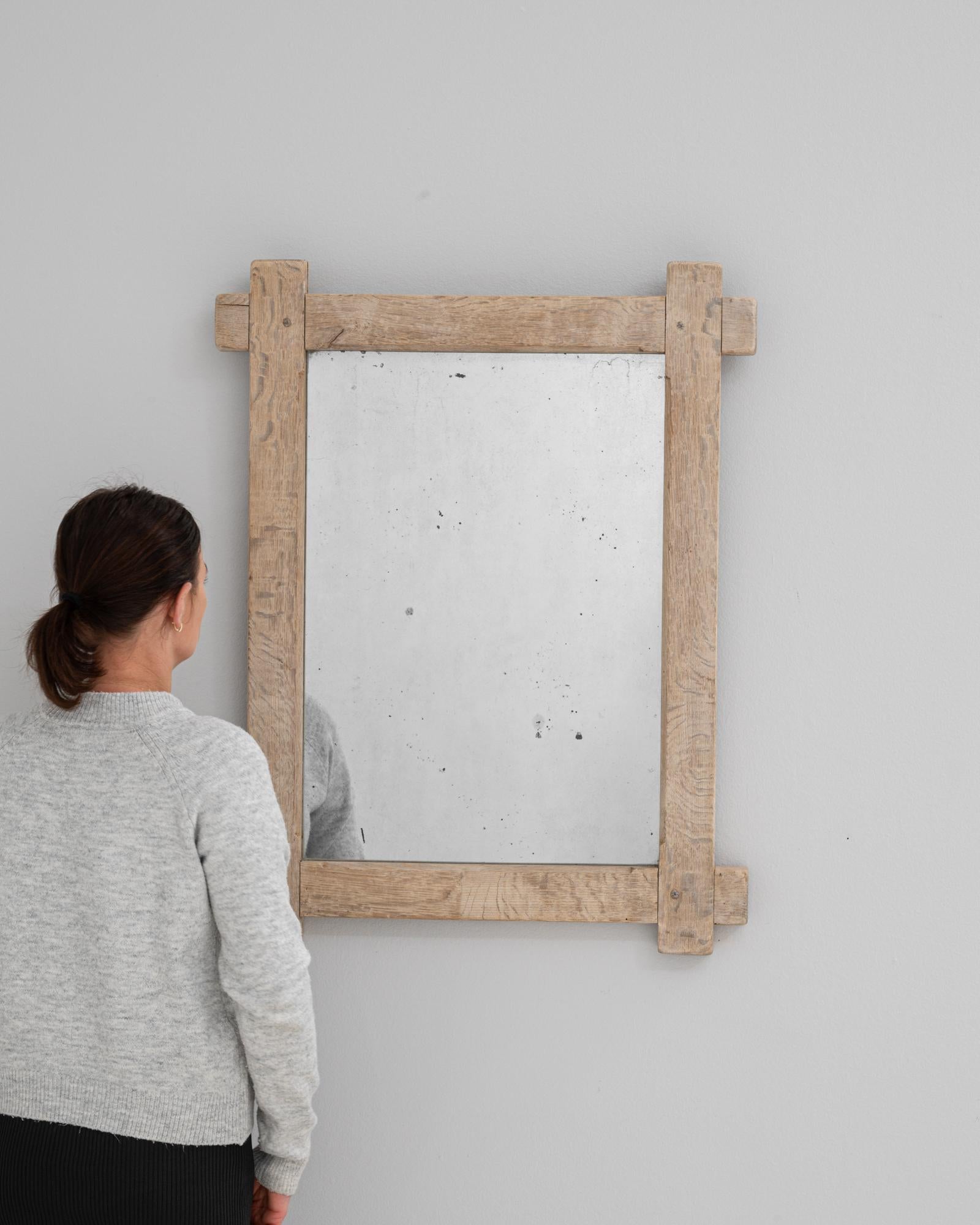 This 20th Century French oak mirror features a robust, handcrafted frame that showcases traditional pegged joinery and raw, natural texture. The oak's warm tone and visibly grained surface emphasize its solid construction, while the aged mirror