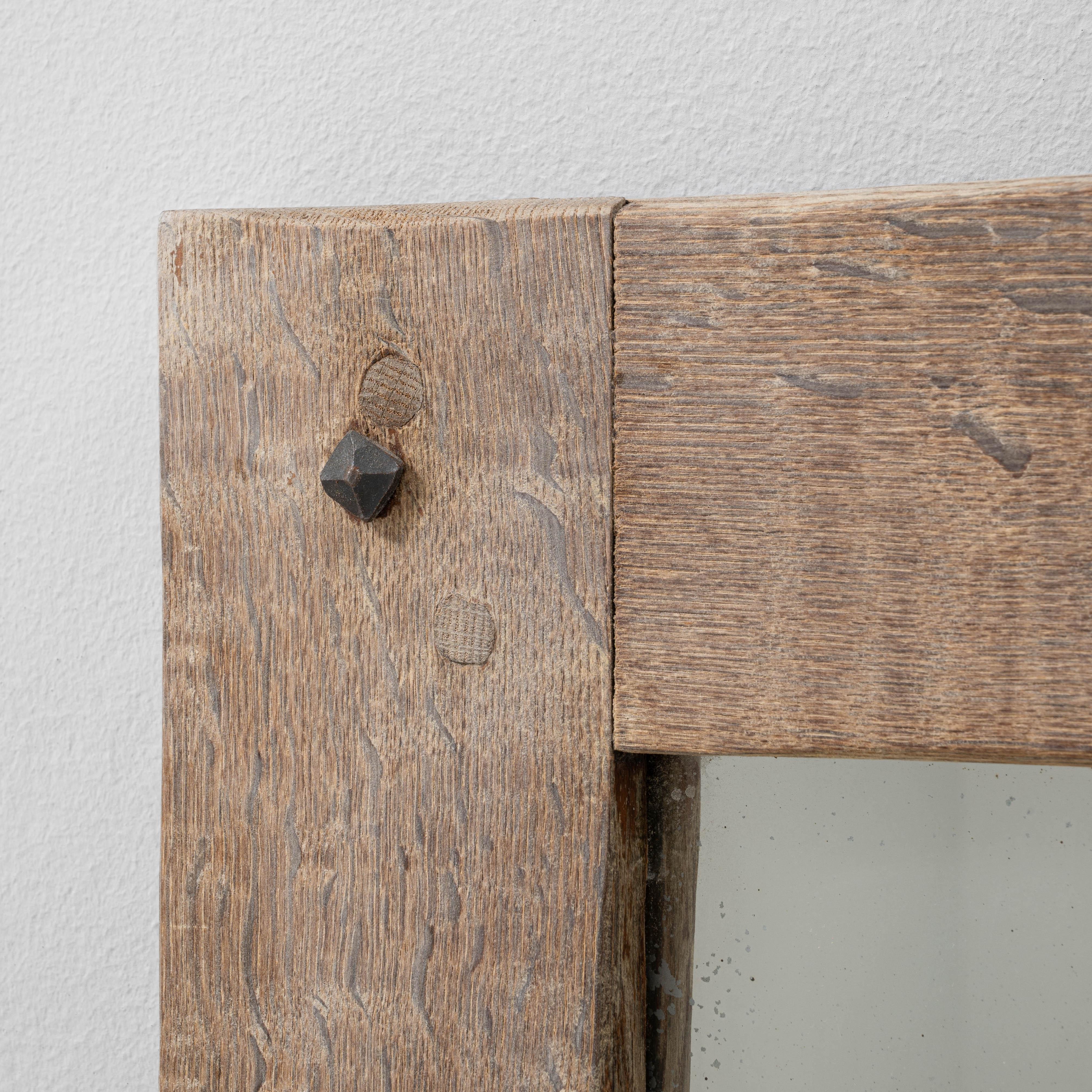 This 20th century French oak mirror features a simple, rustic design that highlights the natural beauty and grain of the wood. The solid oak frame, constructed with visible joinery and aged patina, reflects traditional French craftsmanship rooted in