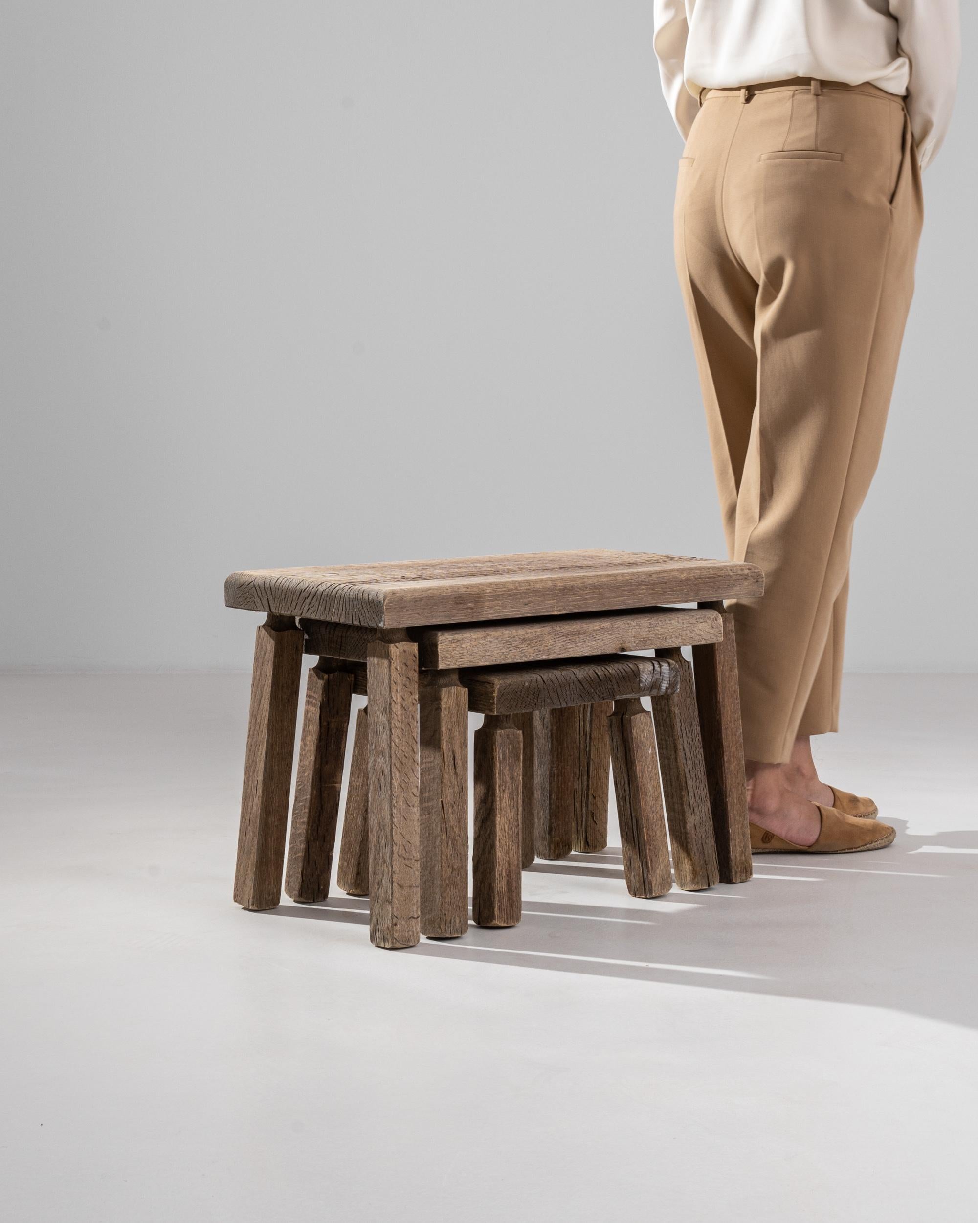 A set of vintage French nesting tables, rustically rendered in oak. This set of three, smartly tuck underneath one another, suggests potential arrangements. Careful lathing at the top of each leg indicates expert craftsmanship, while the rough