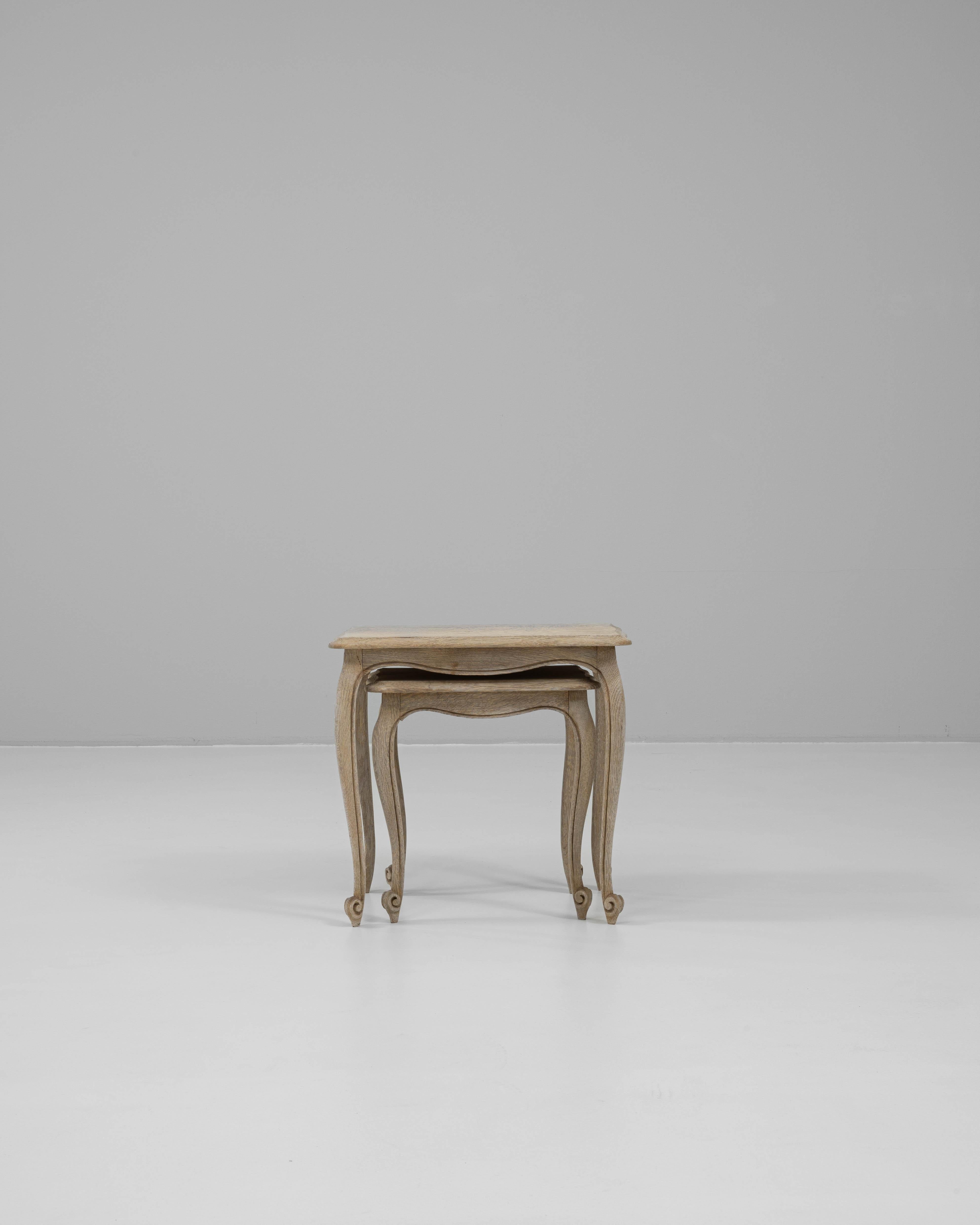 20th Century French oak nesting tables featuring a graceful pair of matching forms with cabriole legs and scalloped aprons. Crafted from solid oak with a softly bleached finish, these tables highlight the elegance and lightness of French provincial