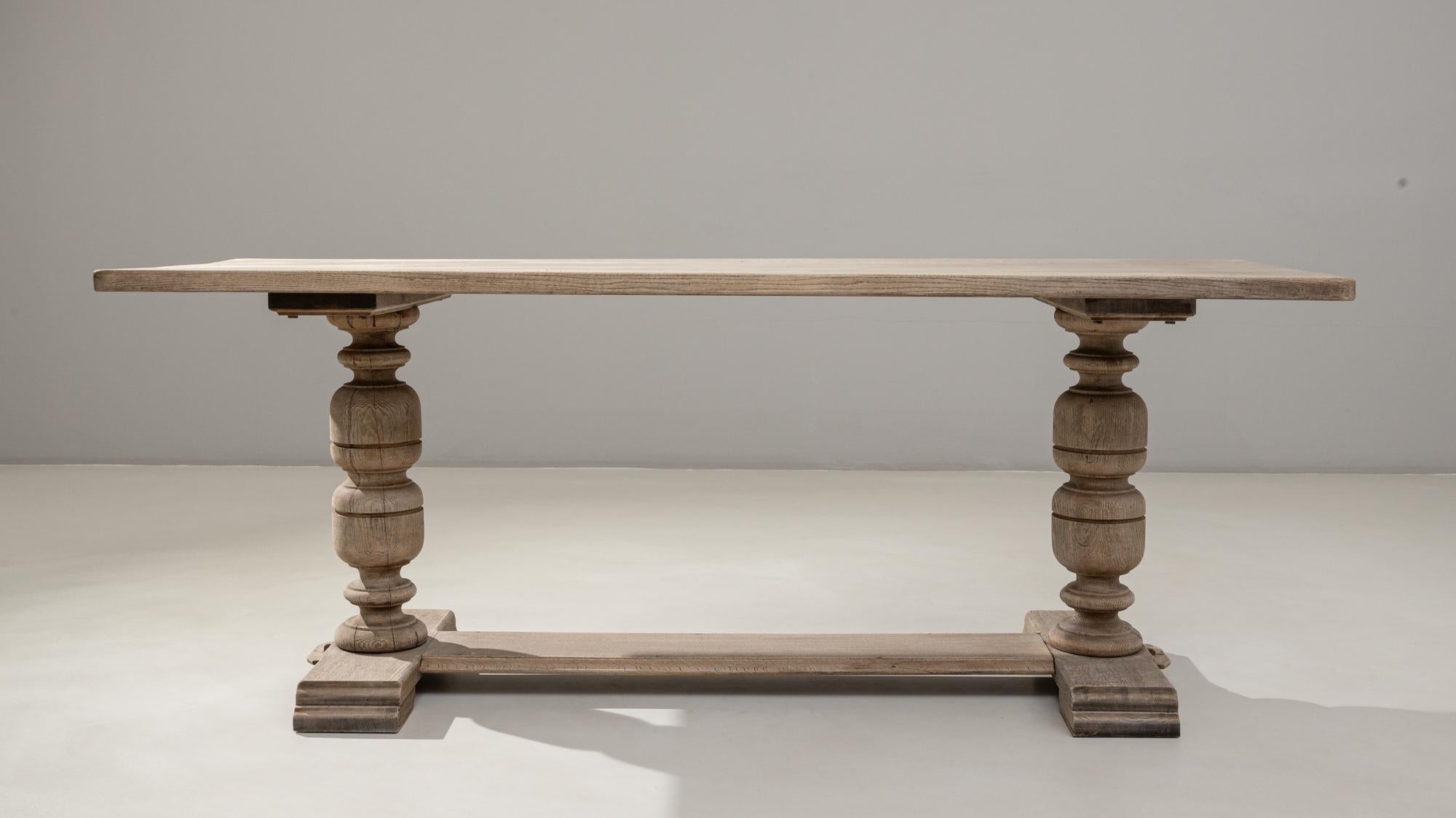 Cette table de salle à manger à tréteaux en chêne français du XXe siècle présente un long plateau rectangulaire soutenu par deux importants pieds tournés en balustre, reliés par un large châssis central. Fabriqué en chêne massif, il présente une