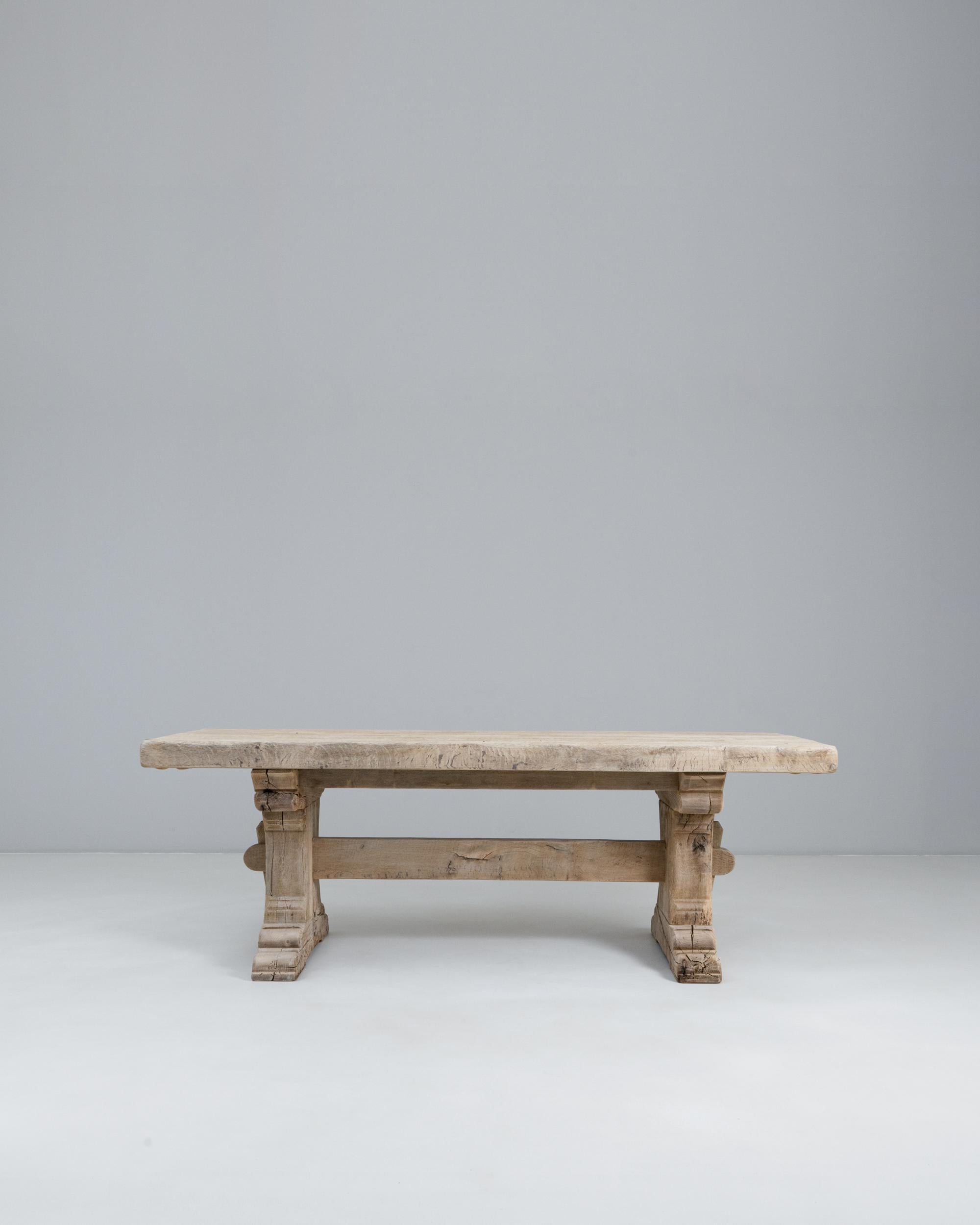 This 20th Century French oak trestle dining table showcases timeless craftsmanship and a bold, rustic presence. The thick, solid oak top features a naturally weathered surface with visible grain patterns, tool marks, and gentle irregularities that