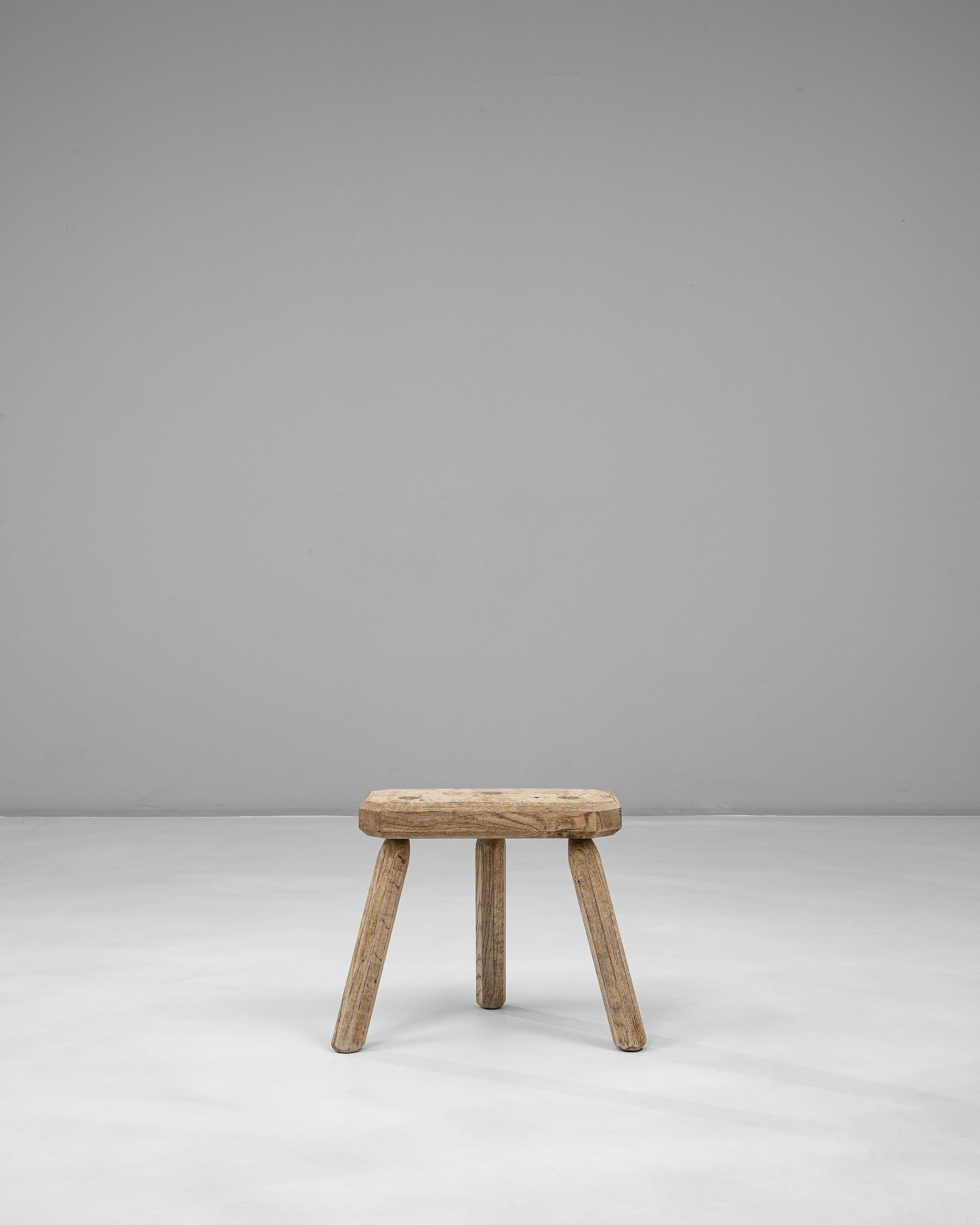 Ce tabouret tripode en chêne français du 20e siècle présente une forme rustique d'une grande simplicité, façonnée par un travail artisanal pratique. Son assise épaisse, taillée à la main, présente des marques d'outils visibles, des bords adoucis et