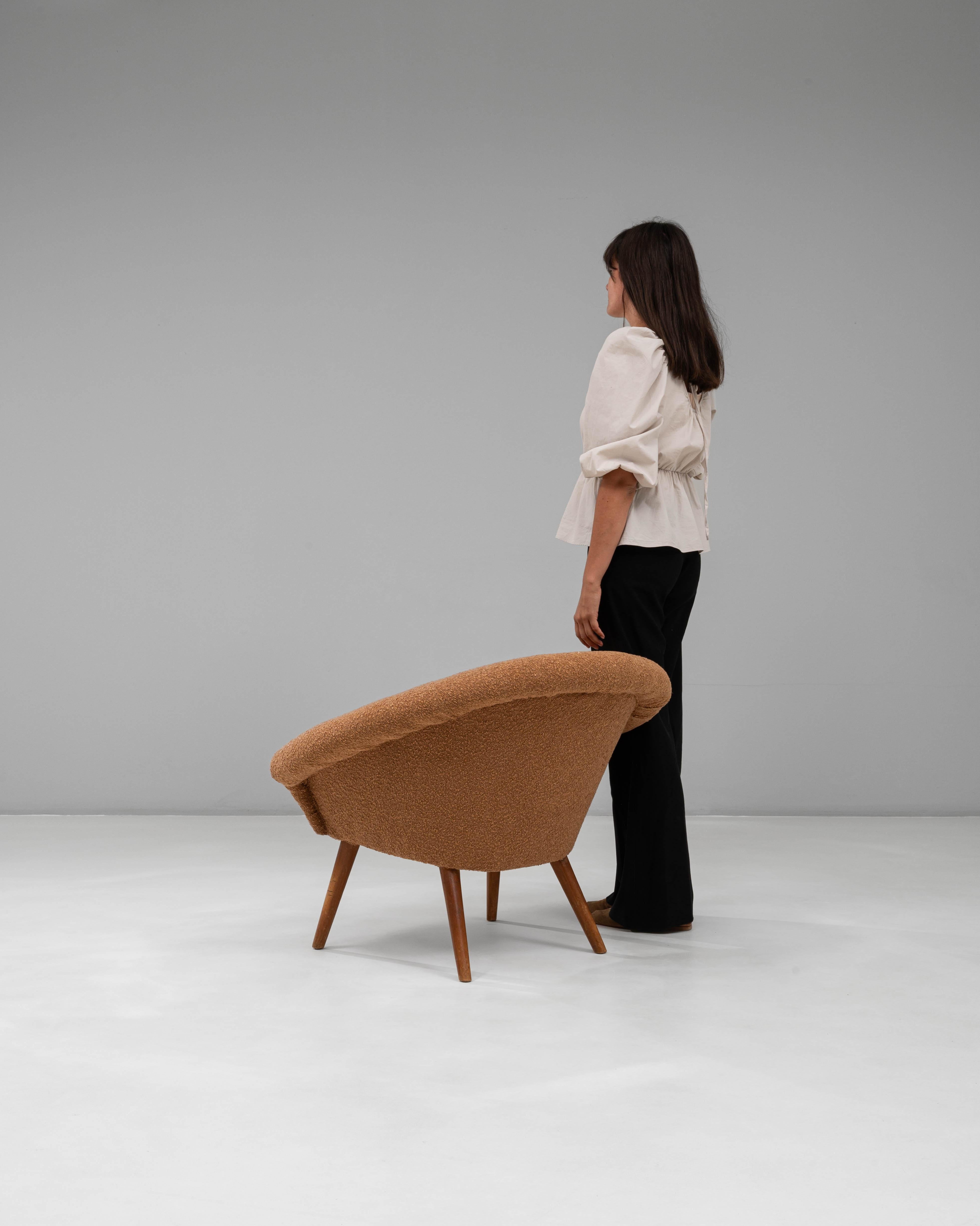 Questa poltrona imbottita in arancione francese del XX secolo presenta un'affascinante silhouette di metà secolo definita dallo schienale arrotondato e avvolgente e dalle gambe affusolate in legno. Il tessuto arancione caldo, con la sua finitura