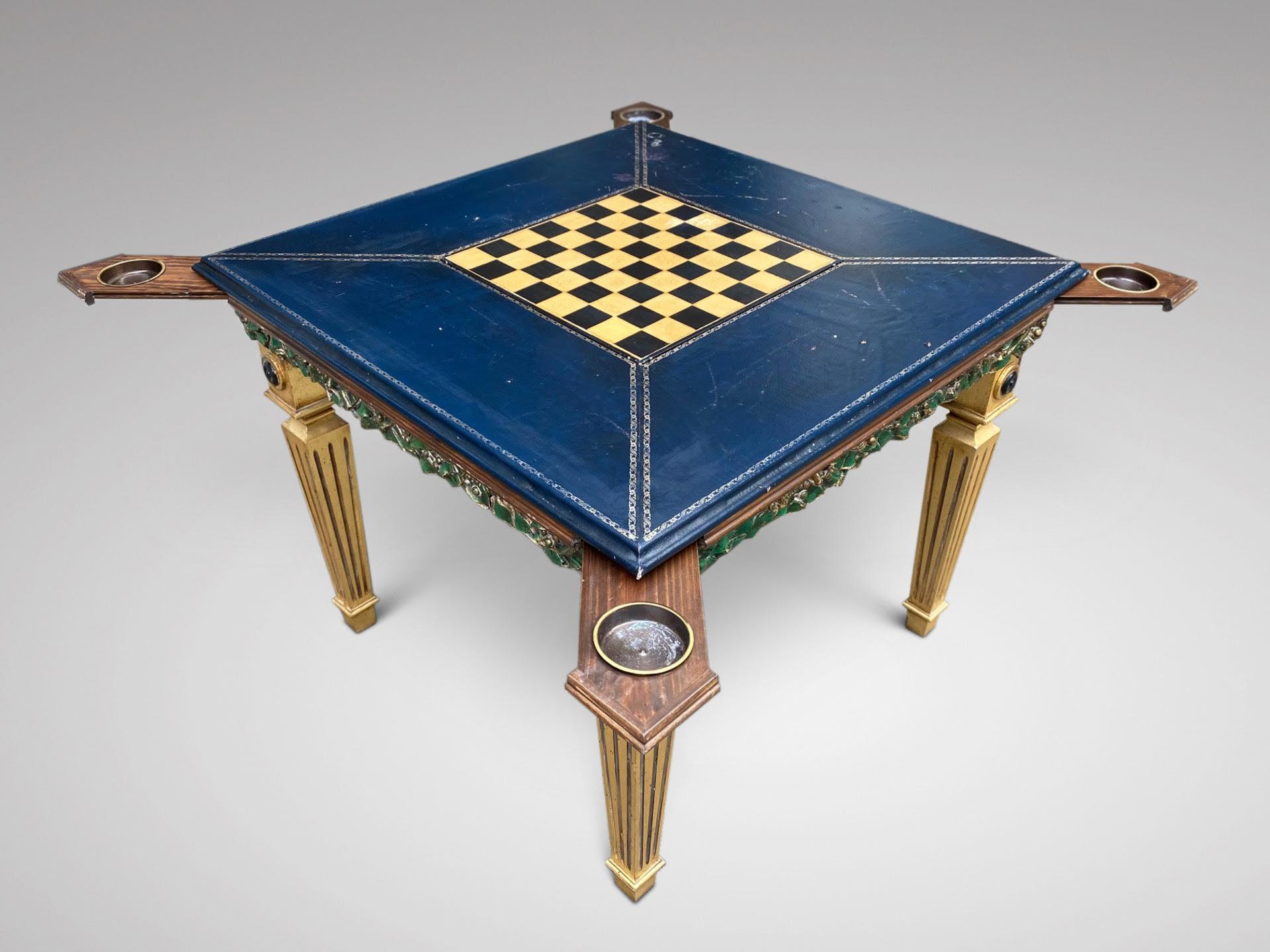A decorative 20th century painted games table with blue tooled leather top with a drop middle and chess board, above a green painted frieze comprising two drawers and four pull out trays to each corner, all standing on four gilt square reeded