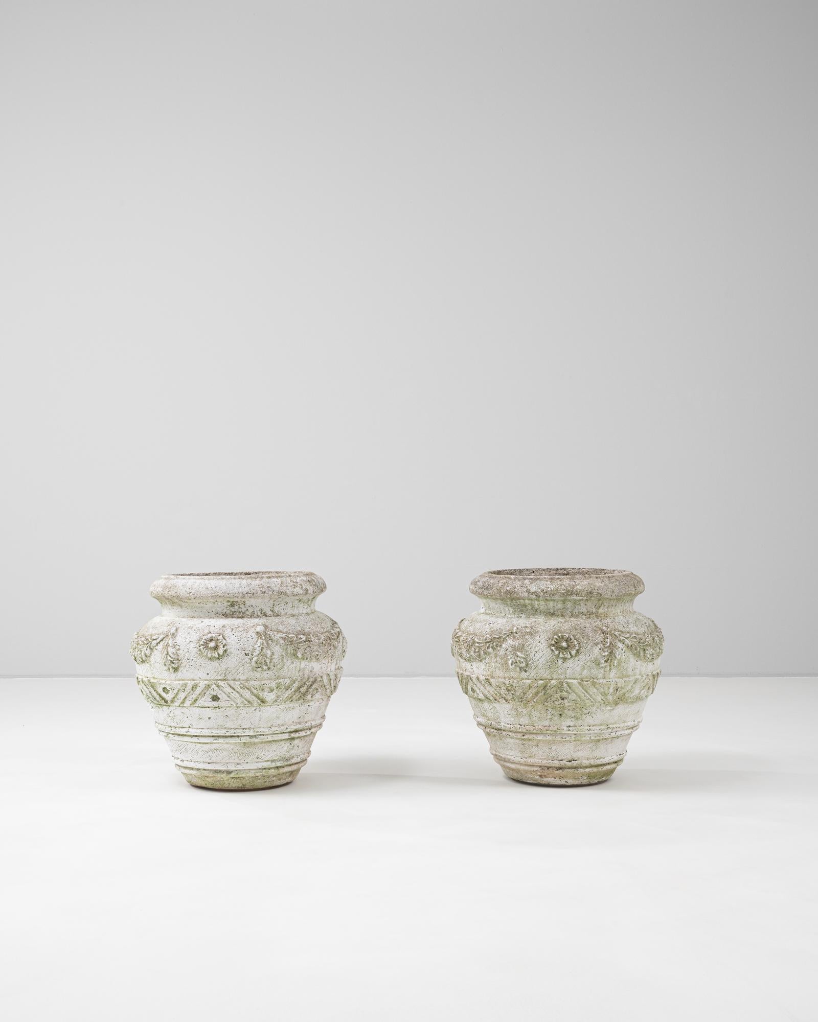 This pair of 20th Century French concrete planters features a bold, sculptural form enriched by deeply carved decorative motifs. Each planter is adorned with stylized floral and geometric reliefs that wrap around the curvaceous silhouette, evoking
