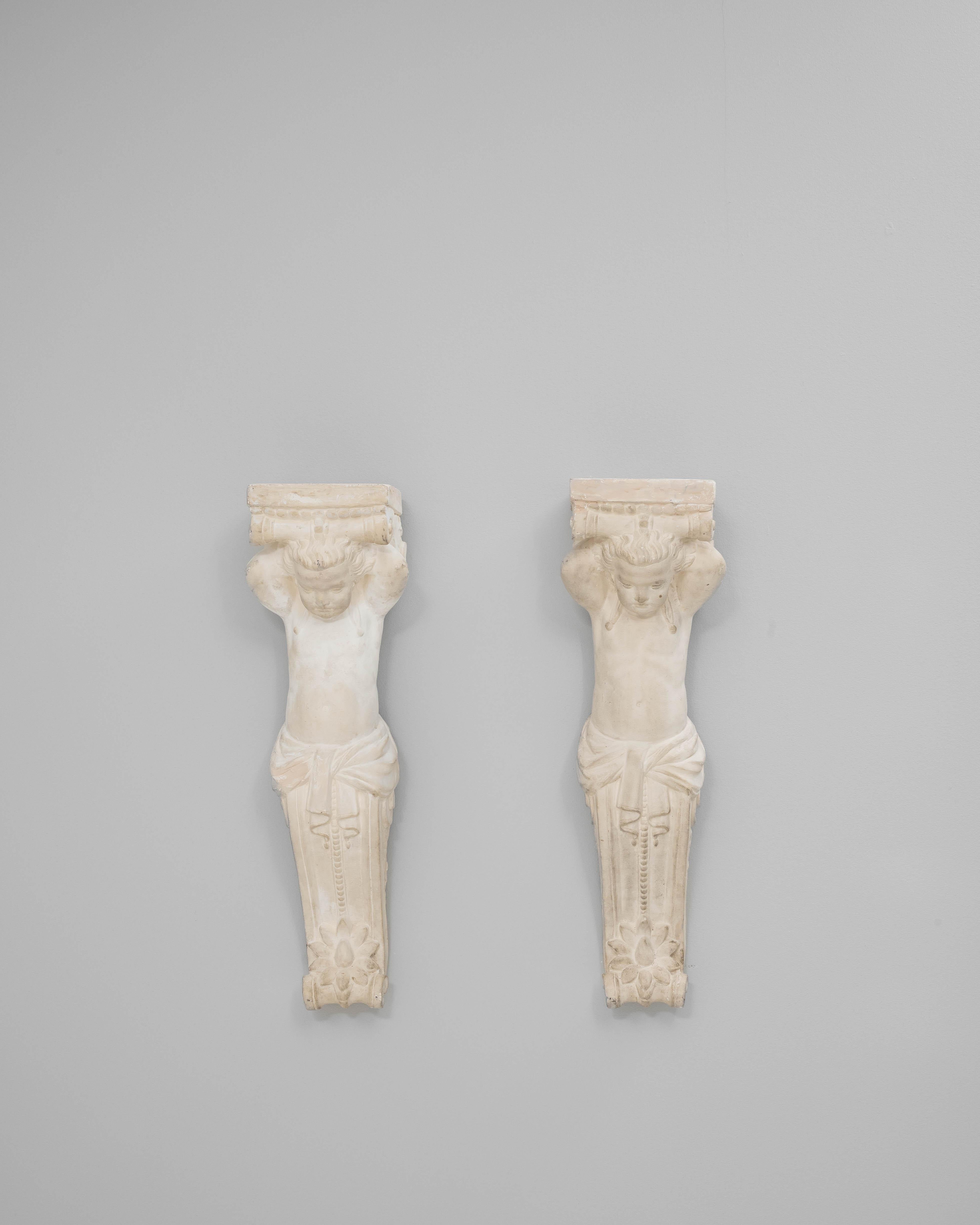 This pair of 20th-century French plaster wall sculptures reflects the neoclassical revival of ornamental design. Each piece depicts a stylized figure reminiscent of ancient architectural caryatids, with finely sculpted details highlighting draped