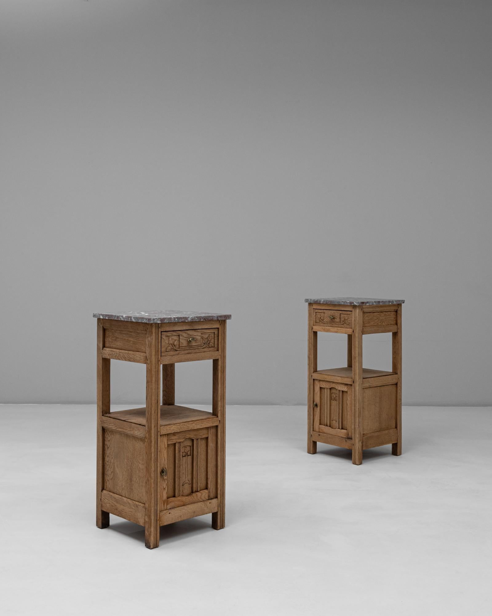 This 20th Century French pair of Provincial oak bedside tables combines rustic charm with refined craftsmanship. Each table features a sturdy oak frame adorned with simple carved details, a lower cabinet door, and a single drawer accented by brass