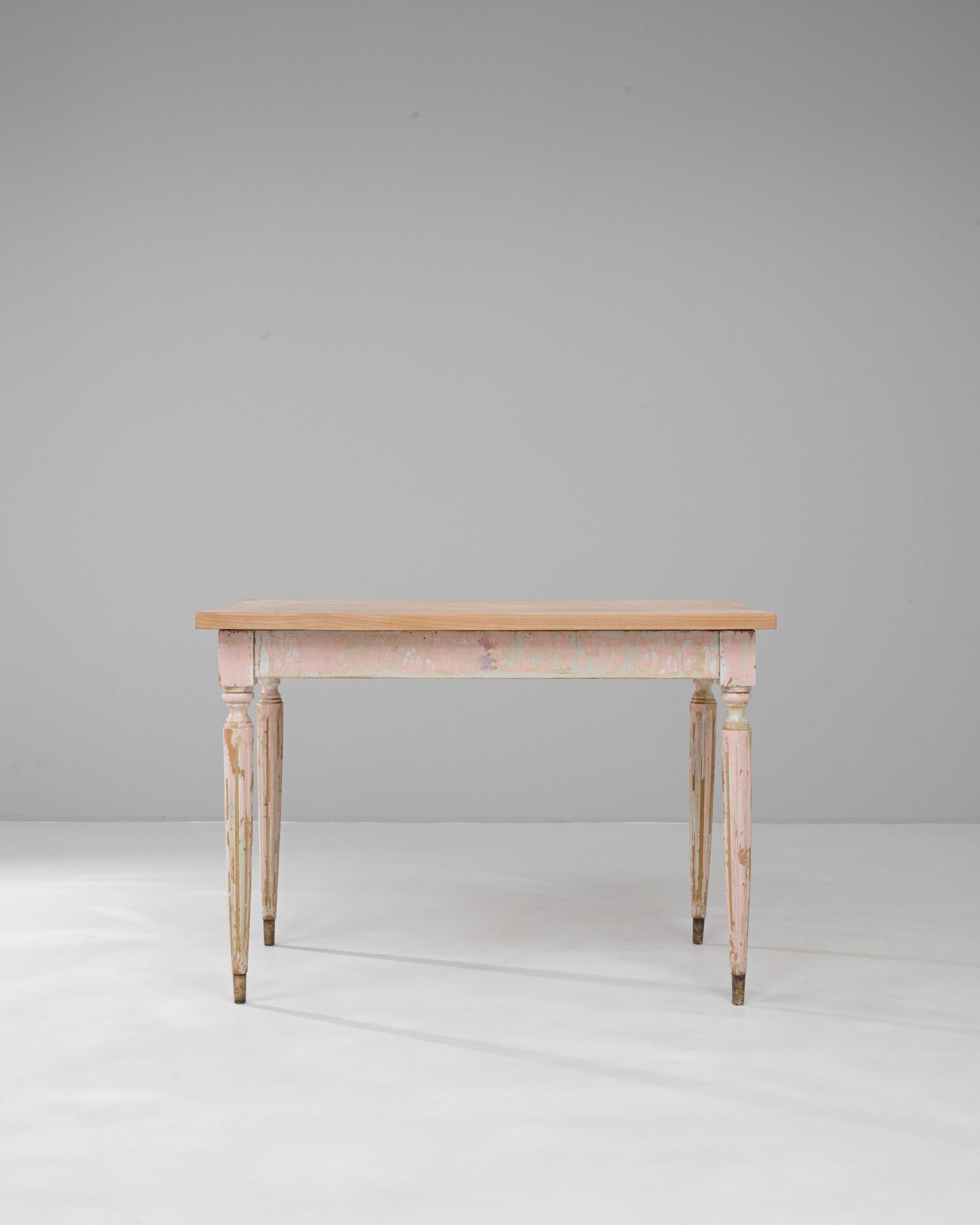 This 20th-century French wooden side table features a beautifully worn patina that reveals layers of soft pink and green paint, giving it an enchanting, timeworn character. The table’s solid wood construction is complemented by delicately turned and