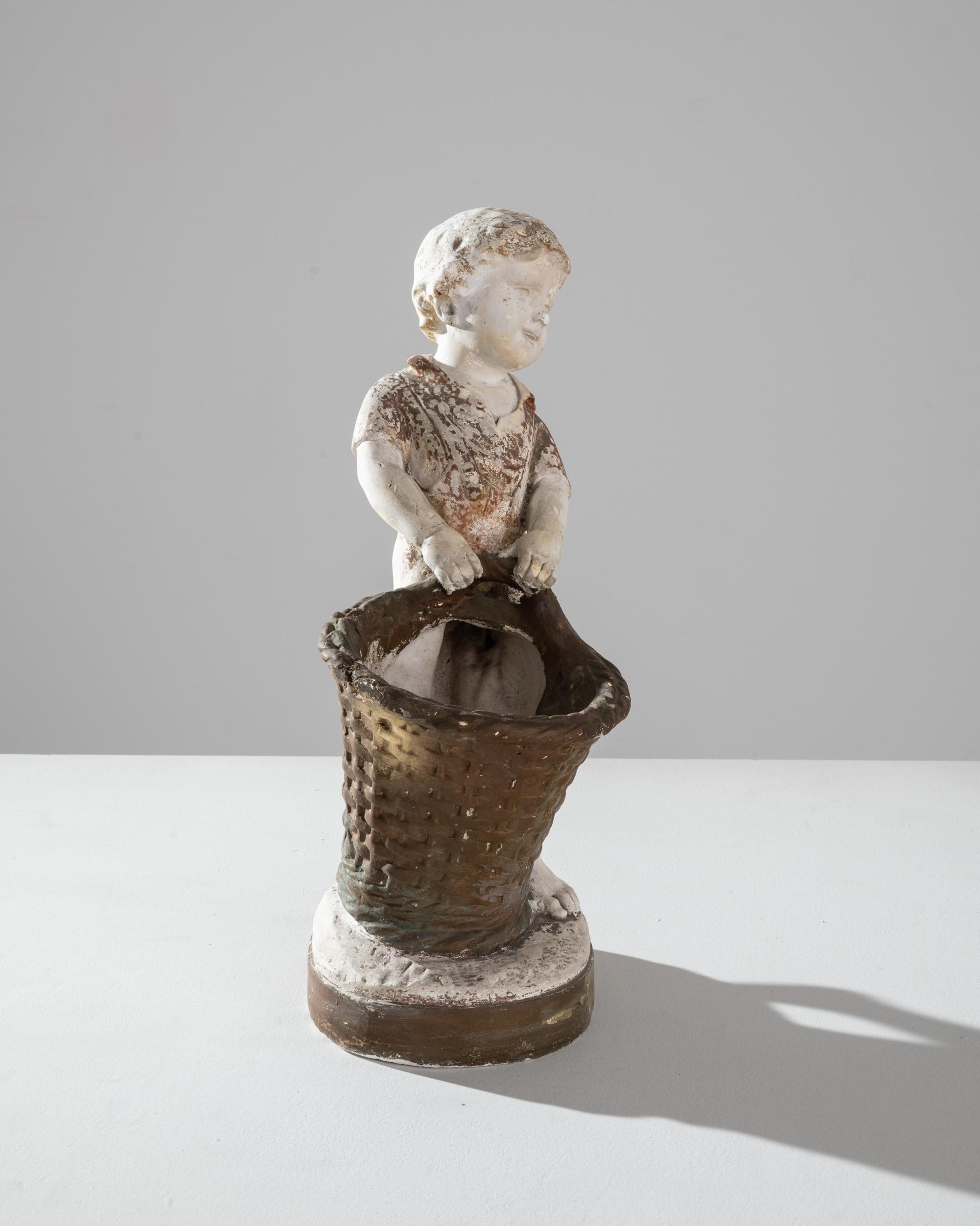 Transport your space to a bygone era with the charm of this 20th-century French Plaster Decoration. The sculpture captures the innocence of youth as it portrays a young boy elegantly bearing a wicker basket. Its antique allure is heightened by a
