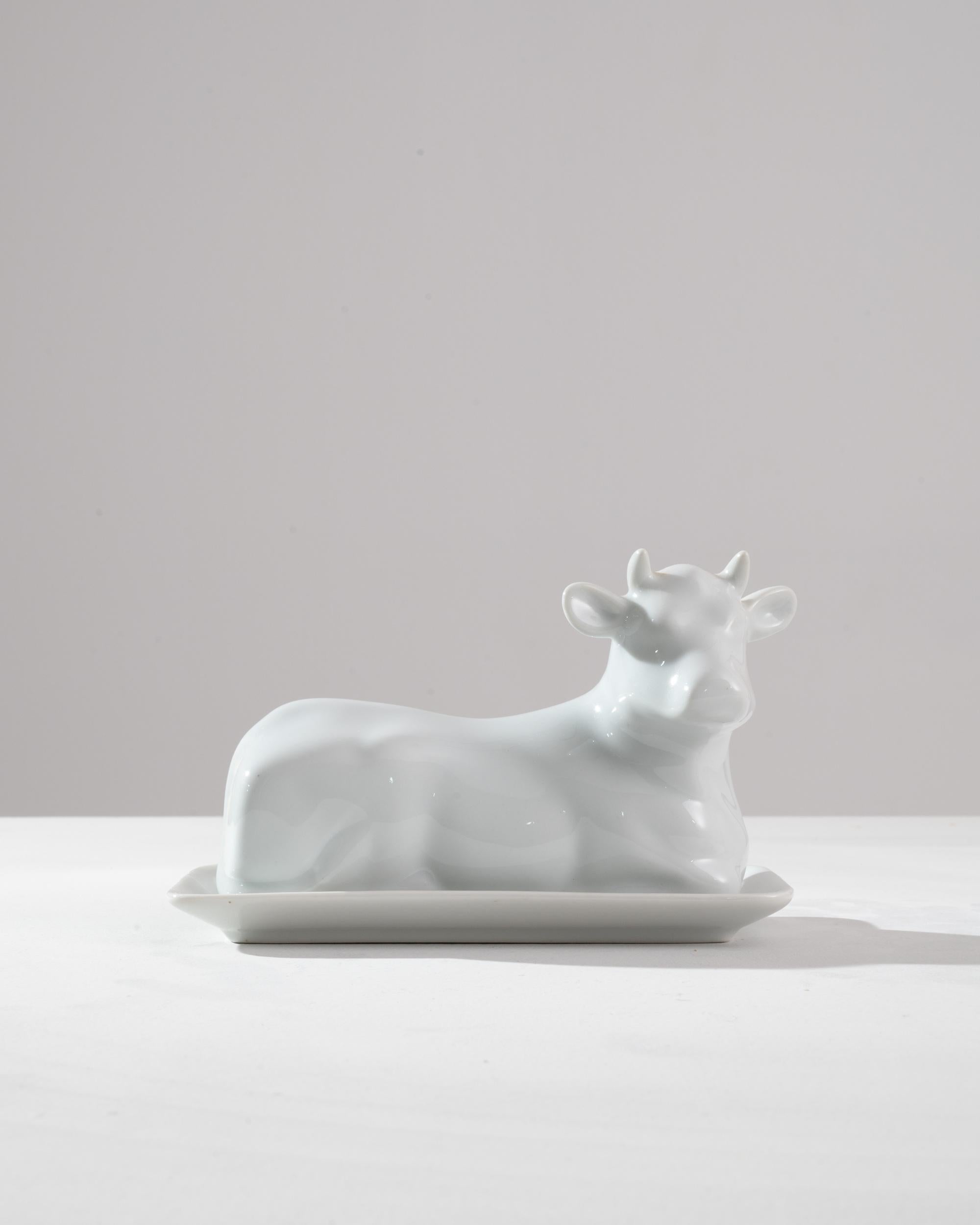 A vintage ceramic butter dish in the shape of a dairy cow. Made in France in the 20th century, this piece is a paean to the artistry of French butter-making. The cow rests in a peaceful, contented position; her little horns and wide ears are