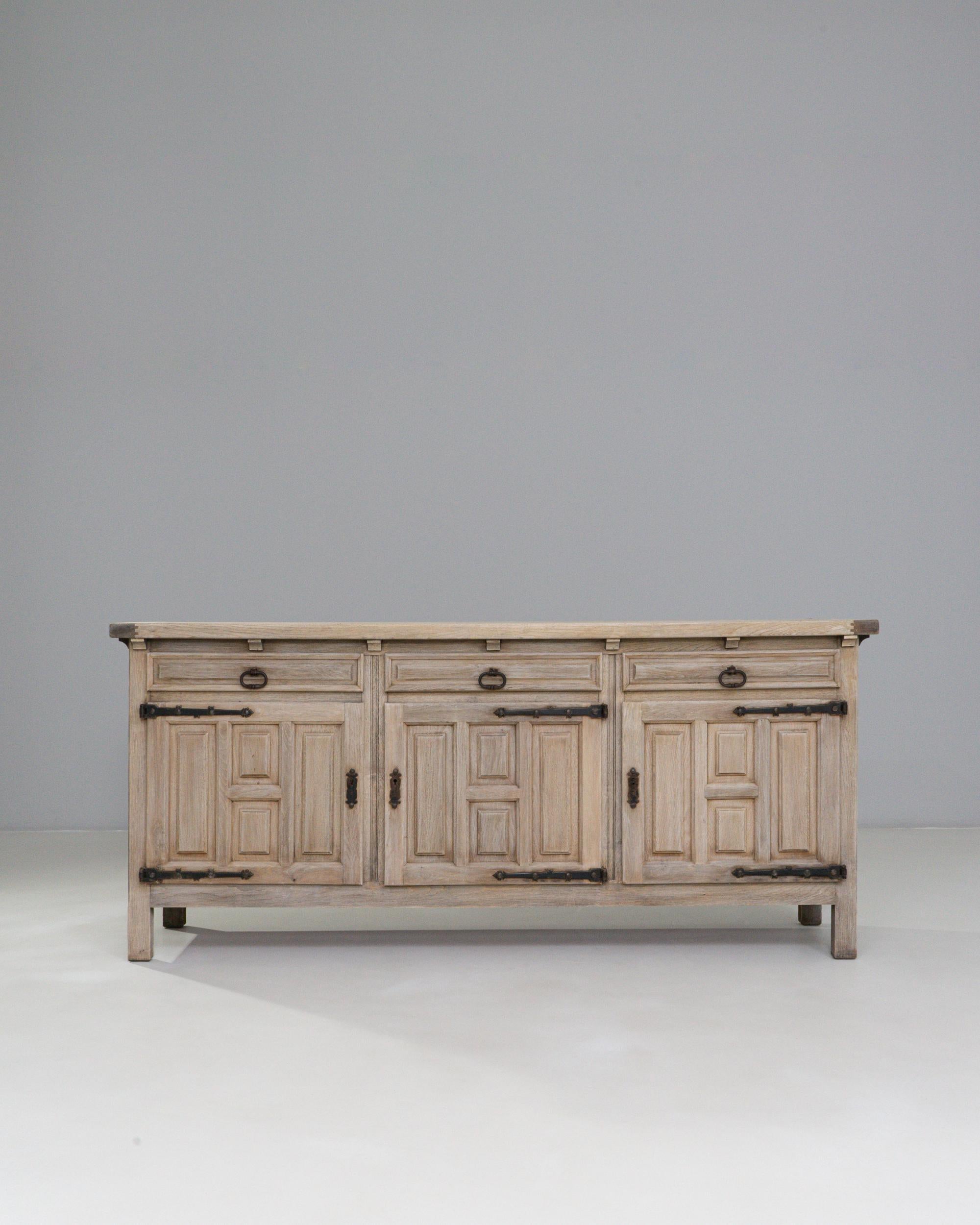 20th Century French Primitive Oak Buffet With Iron Hardware. This substantial French buffet reflects the honest craftsmanship and utilitarian charm of primitive design, constructed from solid oak with a softly weathered, natural patina. The façade