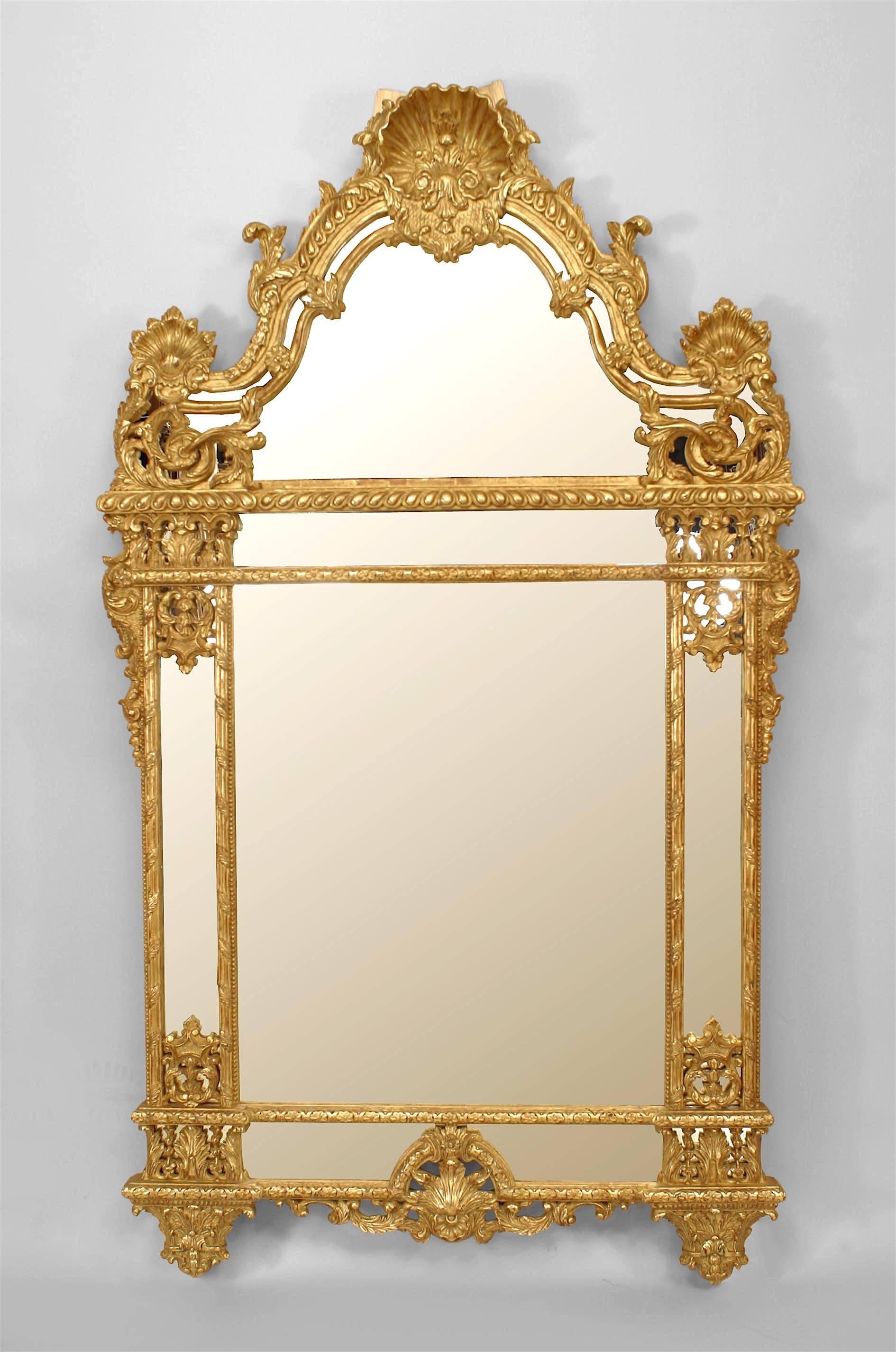 French Regence-style (20th Century) carved giltwood wall mirror with a pediment, side finials, and a shell form filigree carving over mirrored side panels.
