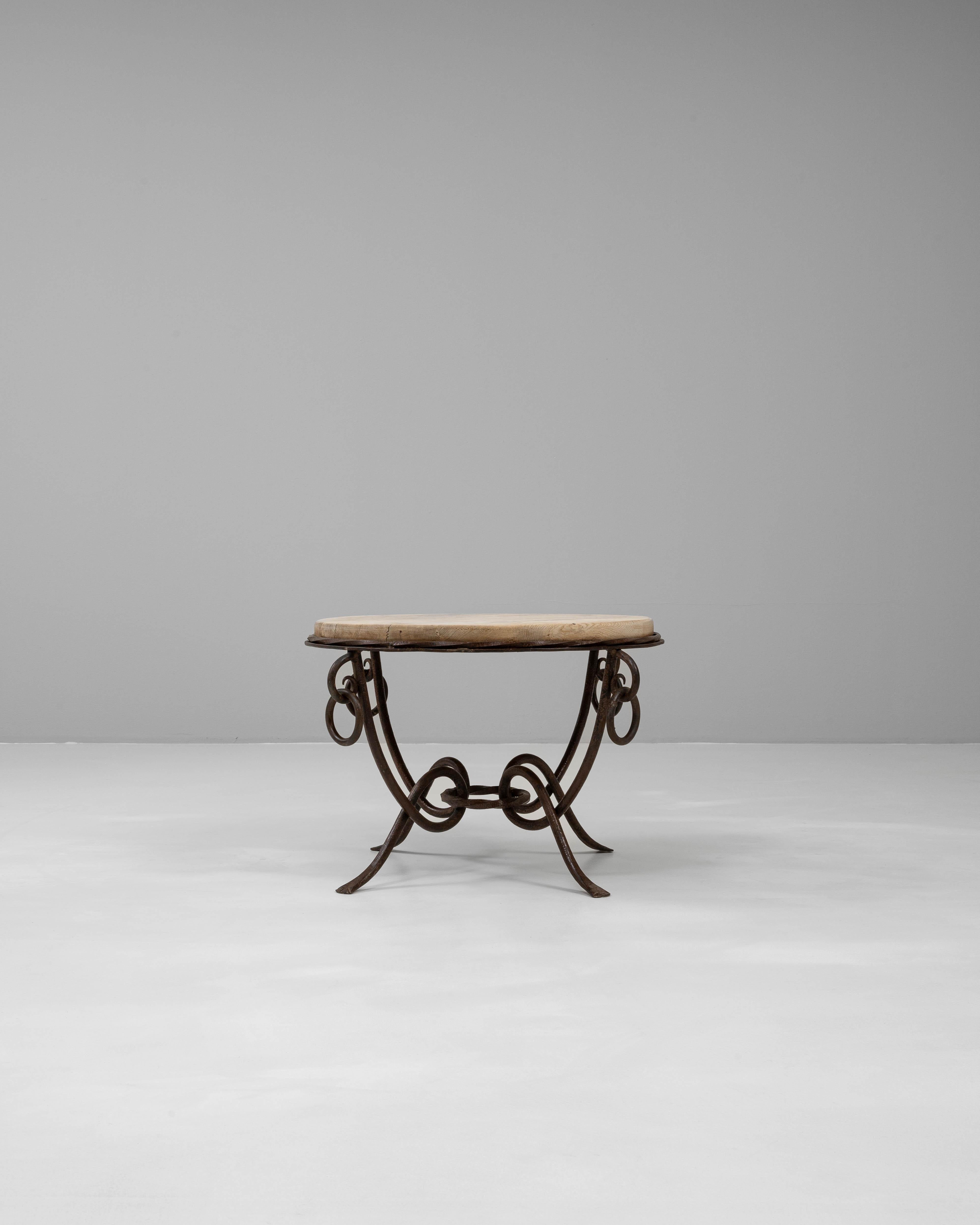 Esta mesa de centro francesa del siglo XX presenta una base de hierro forjado elegantemente forjada con intrincados detalles de volutas y anillas, que ejemplifican la artesanía de la época. La cálida tapa de roble, envejecida con una pátina natural,