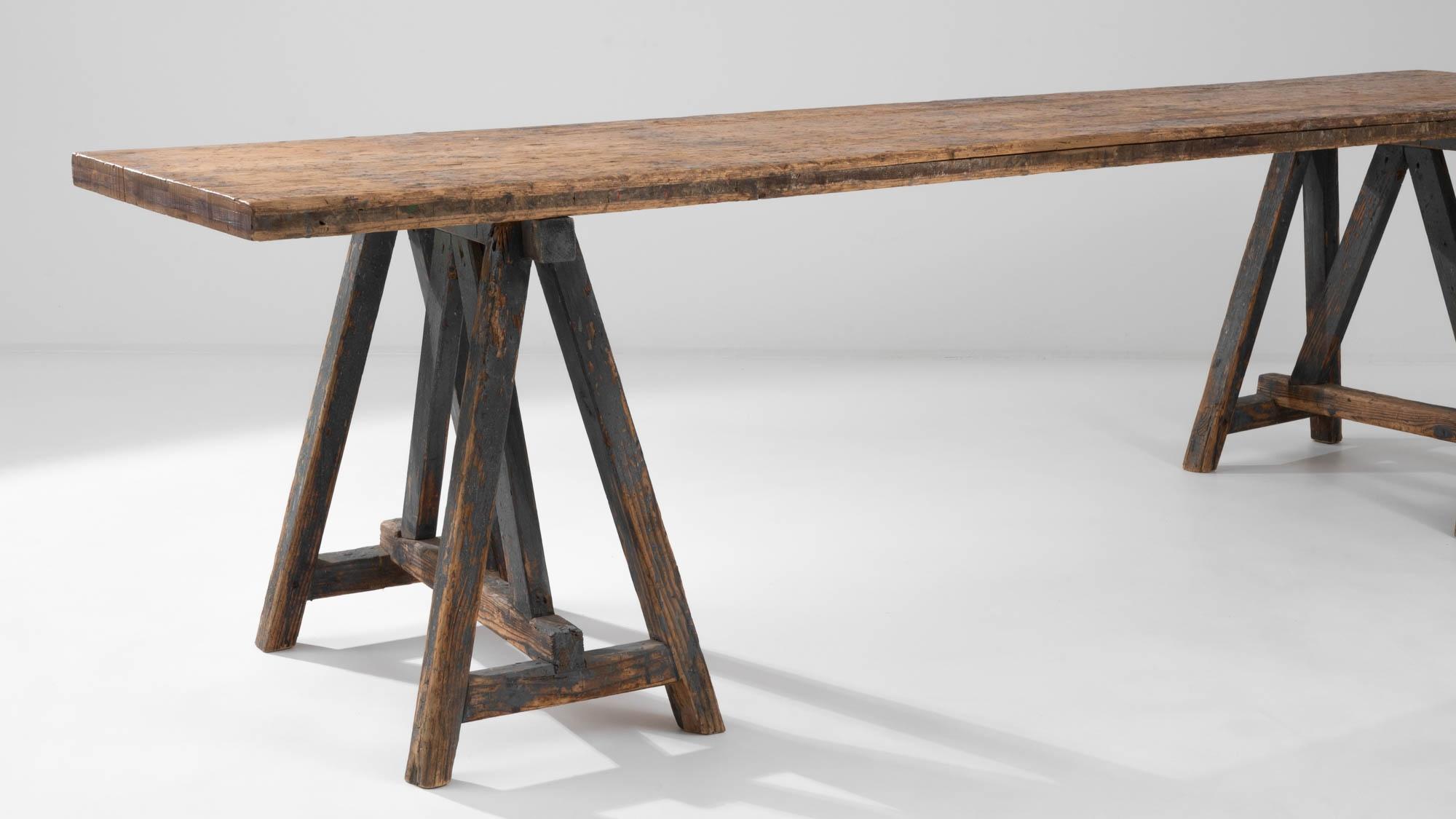 Made in France during the 20th century, this wooden dining table features A-shaped trestle legs, lending it a stylish angular design while providing sturdy support for the plank tabletop. The stripped dark gray-blue finish of the base creates an