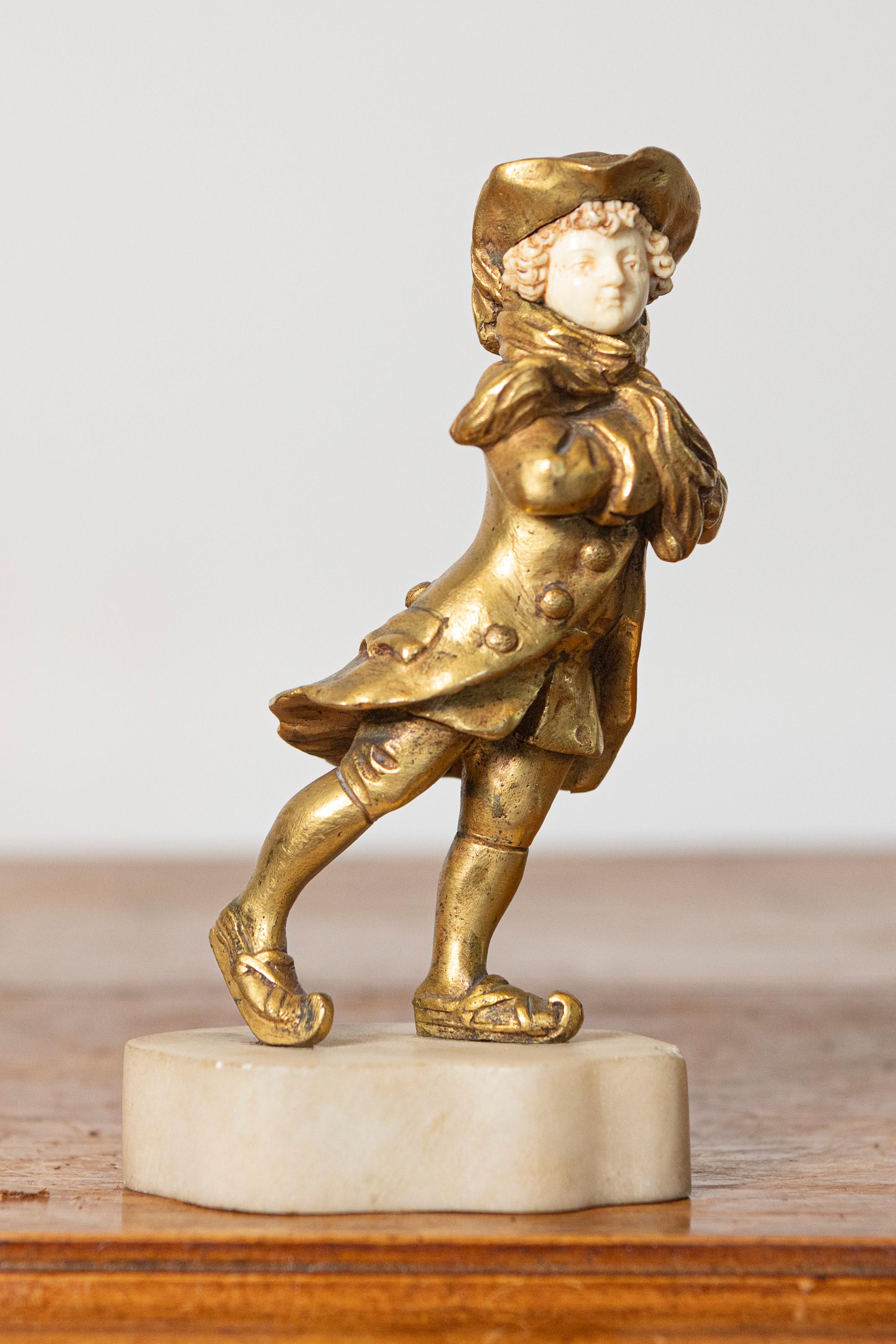 Questa affascinante scultura francese dell'inizio del XX secolo combina l'eleganza del bronzo dorato e i dettagli realistici dell'avorio per creare un pezzo accattivante. Raffigurante un bambino in abiti d'epoca, la scultura è caratterizzata da una