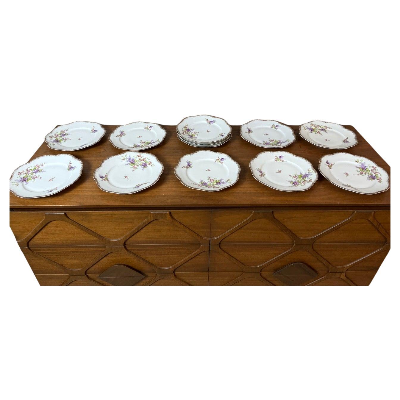 Set of 12 Limoges porcelain dessert plates, a must-have for lovers of fine and elegant tableware. These plates feature a delicate gold trim and a charming countryside floral motif at the center. The scalloped edge adds a touch of refinement and
