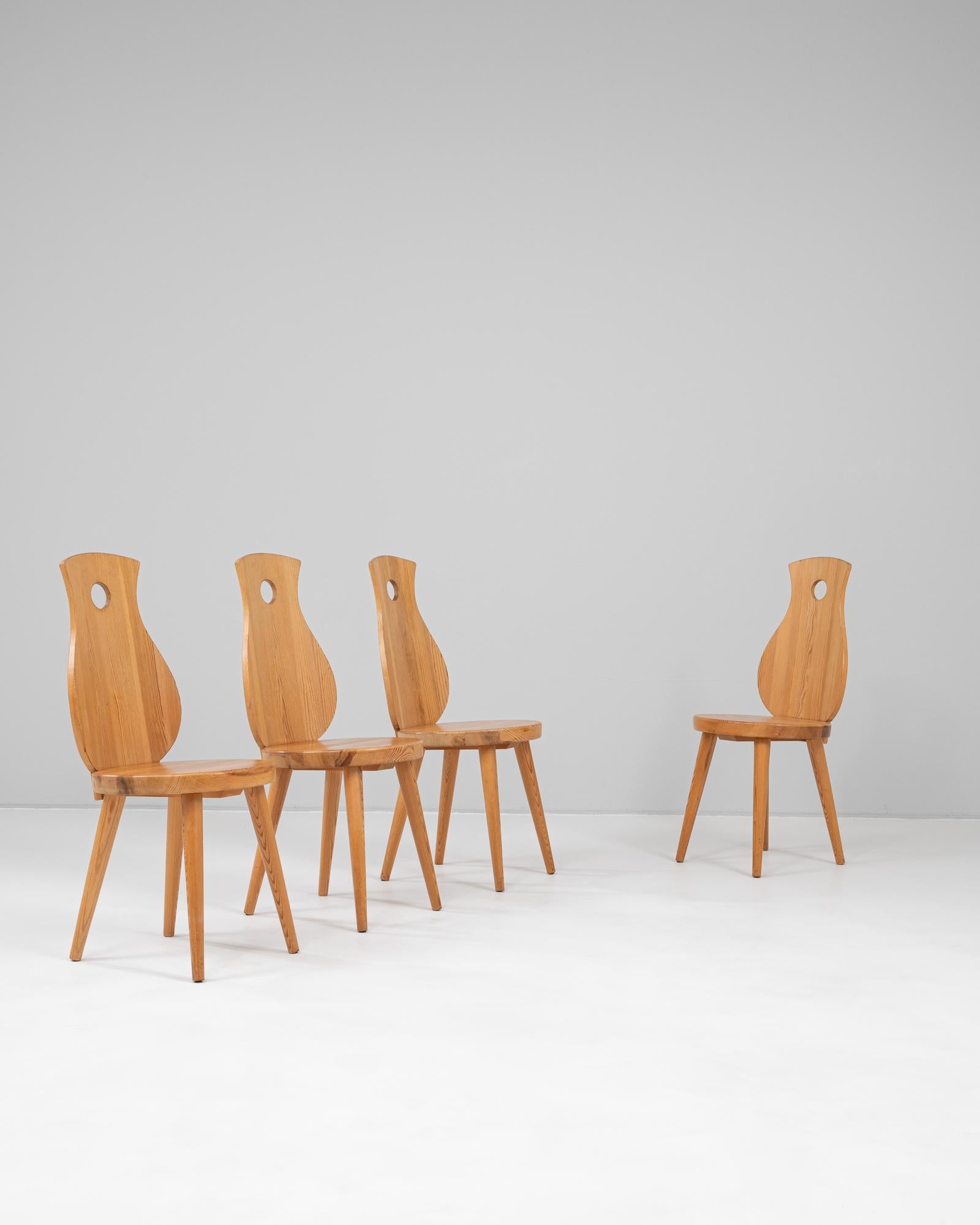 This 20th Century French set of four wooden dining chairs combines whimsical form with solid craftsmanship. Each chair features a sculpted backrest with a gently curved silhouette reminiscent of an artist’s palette or stylized violin, punctuated by