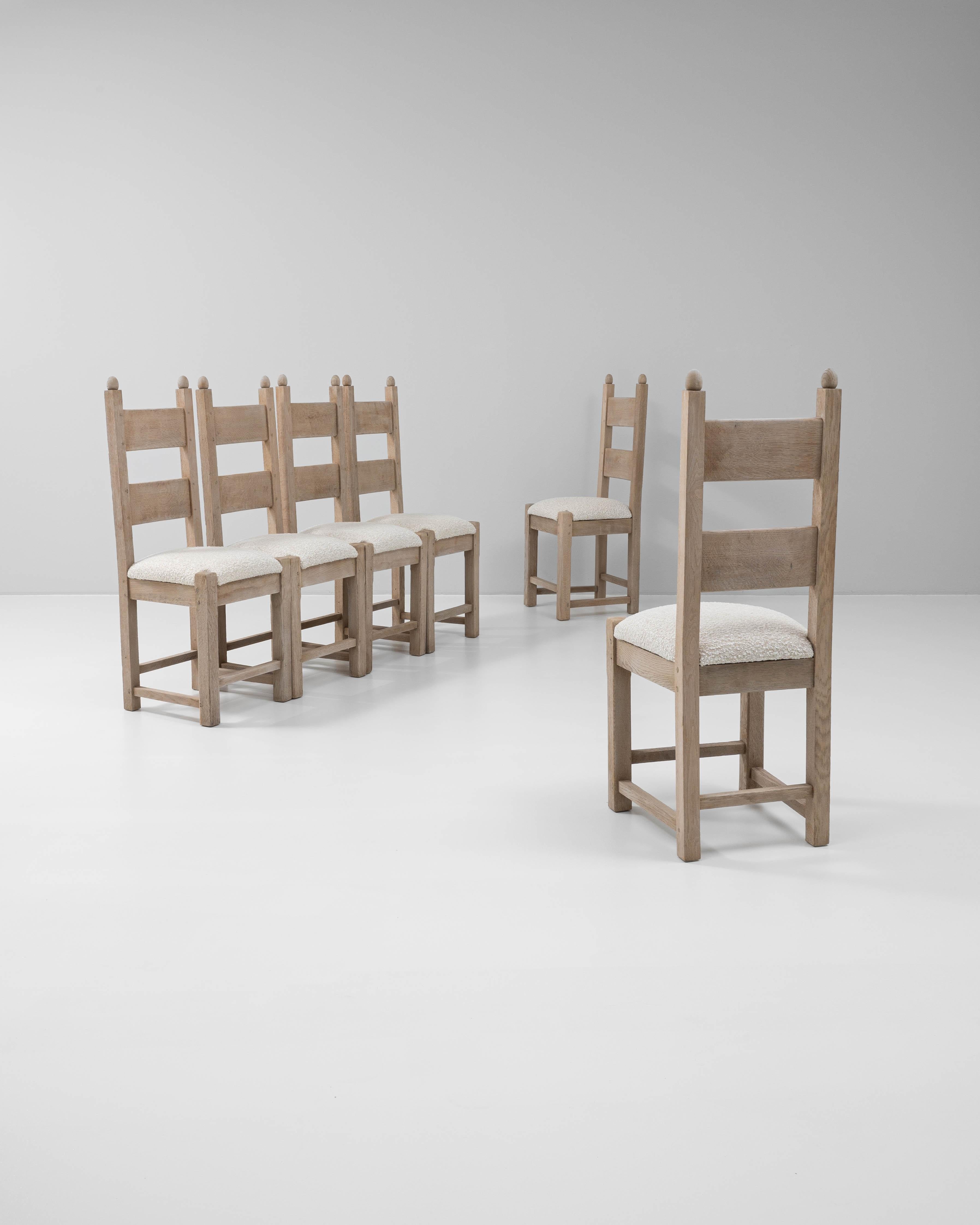 This set of six 20th Century French dining chairs is crafted from solid oak with a gently bleached finish that highlights the wood's natural grain and texture. The high ladder backs are accented with rounded finials, giving the chairs a distinctive