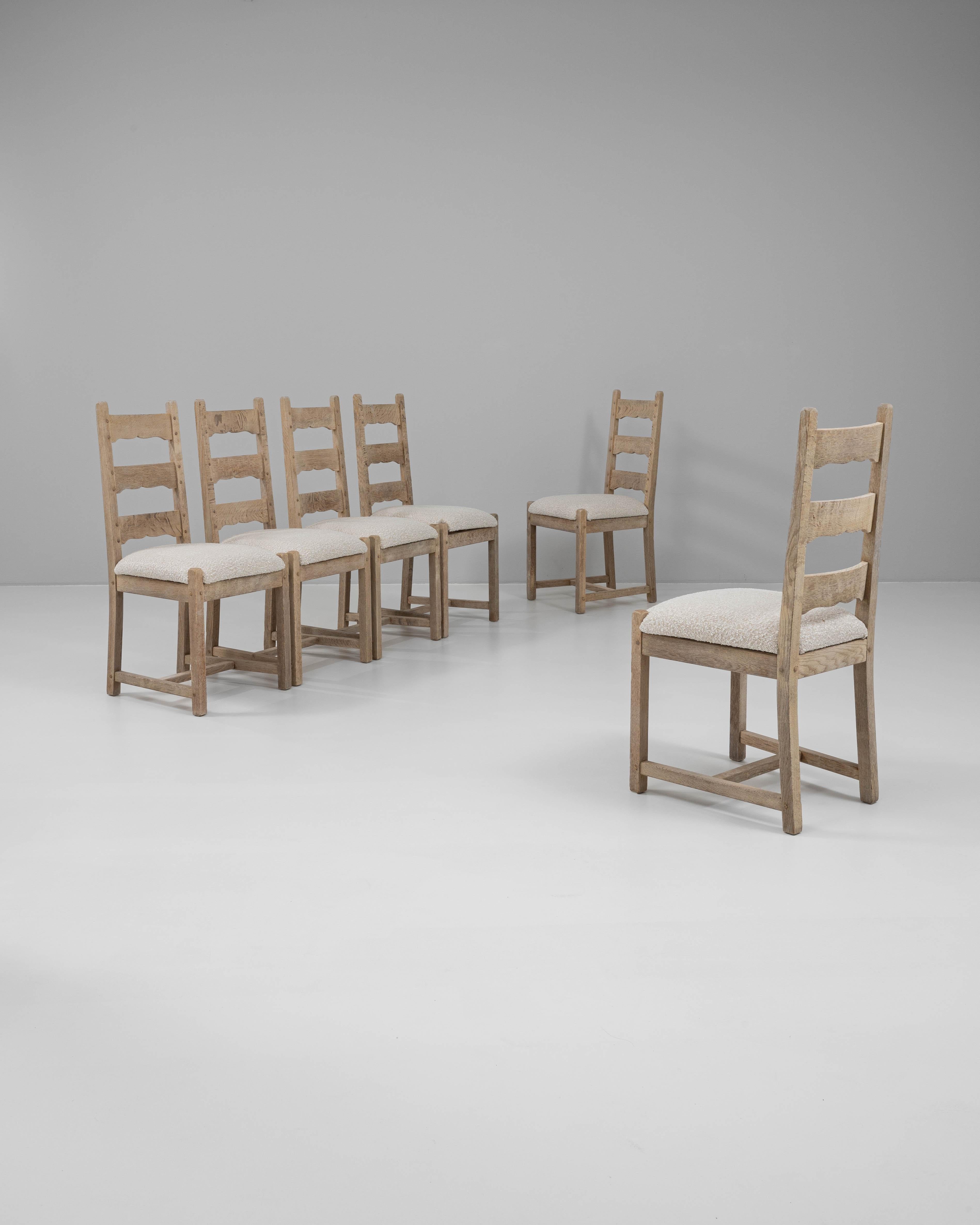 This set of six 20th Century French oak dining chairs features a timeless ladder-back design with subtly curved horizontal slats and square legs connected by stretchers for added stability. Crafted from solid oak, the frames display a softly