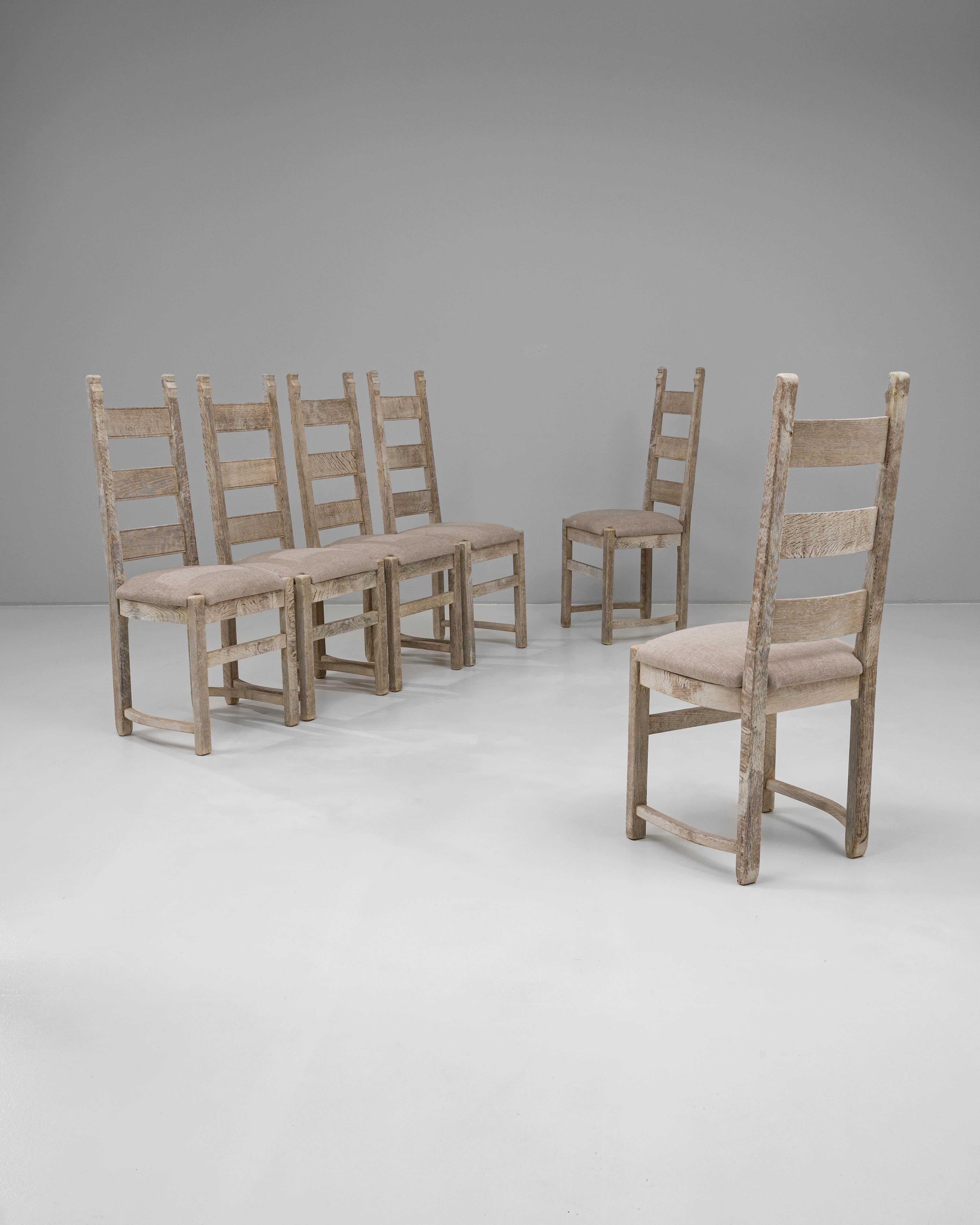 Este conjunto francés del siglo XX de seis sillas de comedor de roble muestra una discreta elegancia con un guiño a la artesanía tradicional. Cada silla presenta un diseño clásico de respaldo en escalera con líneas limpias y un bastidor inferior